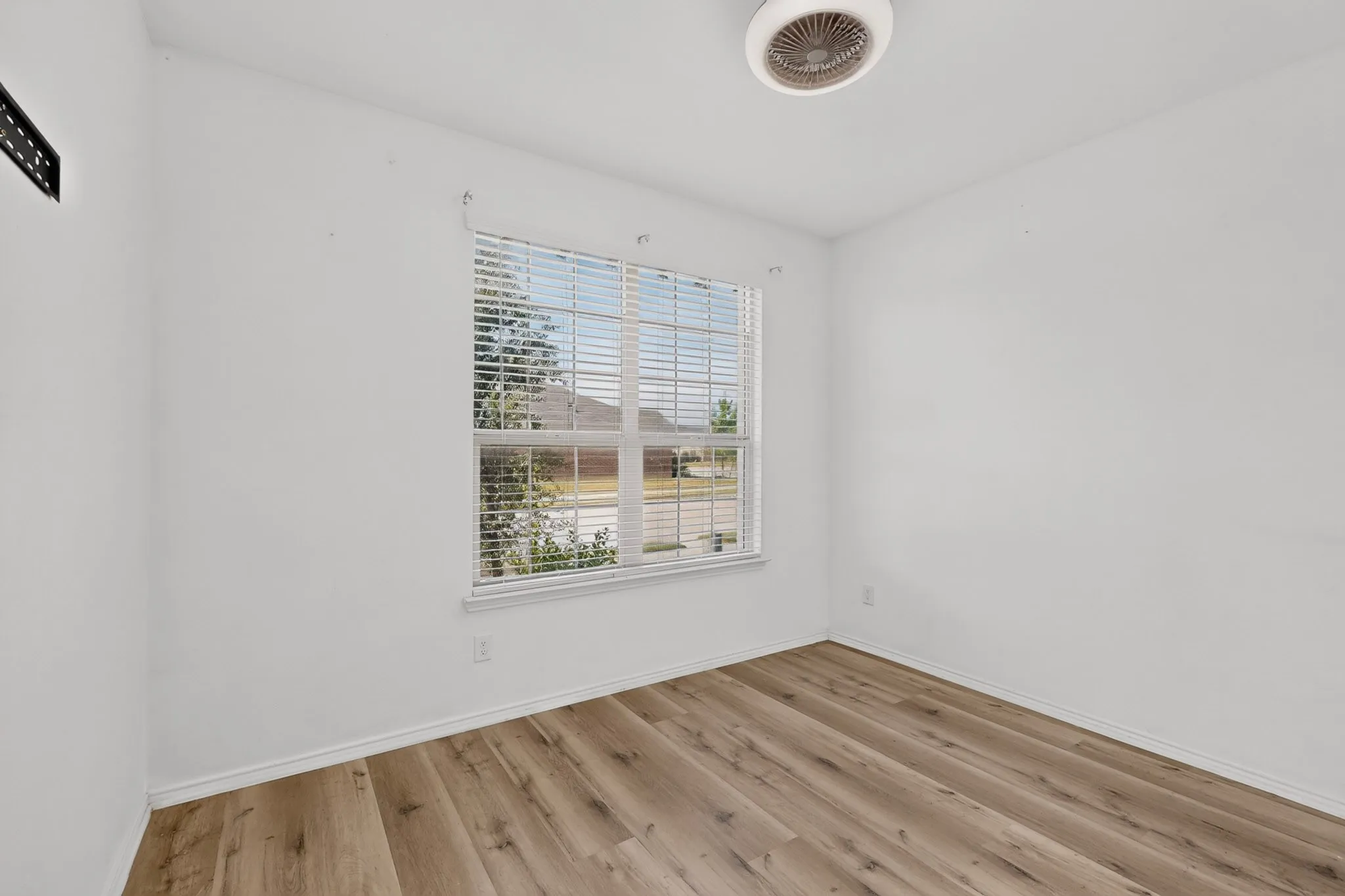 Bright interior space featuring a window with blinds, wood-finish flooring, a ceiling-mounted light fixture, and white painted walls