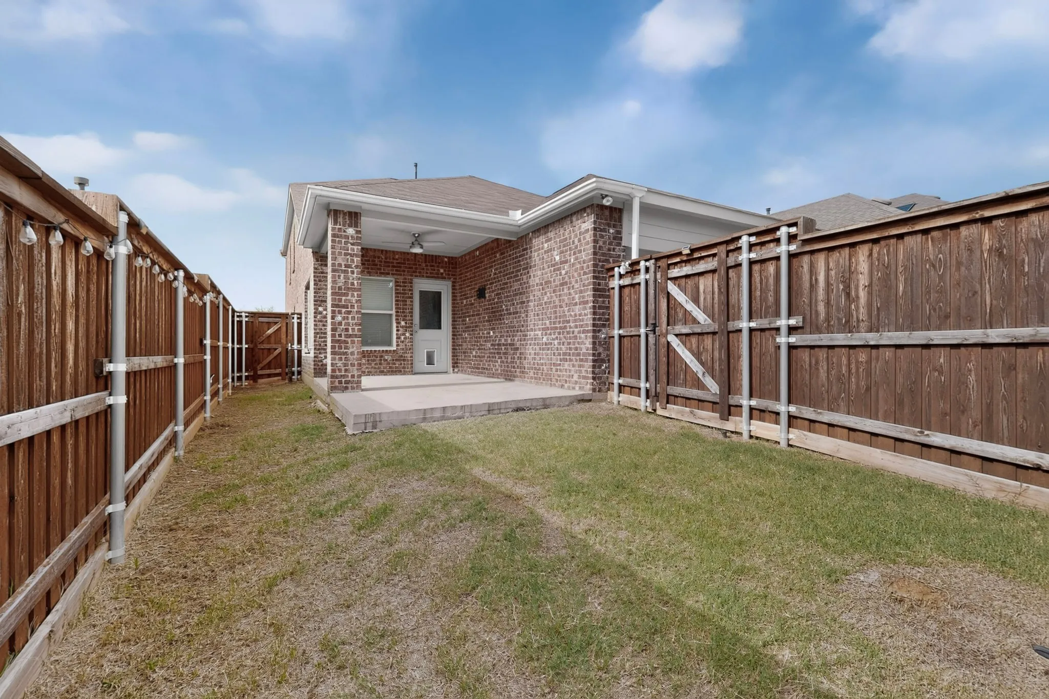 Rear exterior featuring a covered patio with brick columns, an outdoor ceiling fan, and a concrete slab