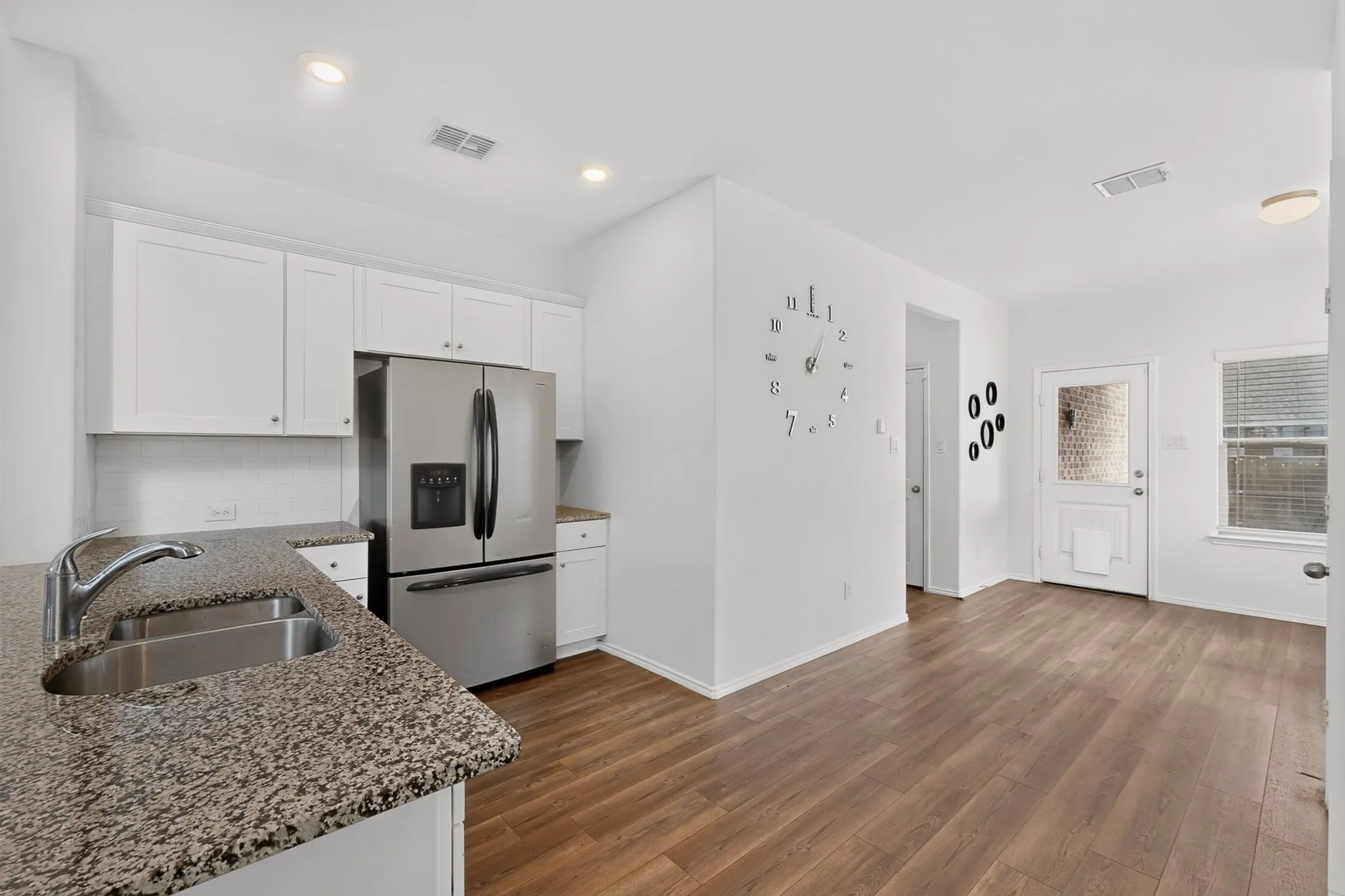 Kitchen area featuring granite-look countertops, a stainless steel double basin sink with a chrome faucet, white cabinetry, and a white subway tile backsplash