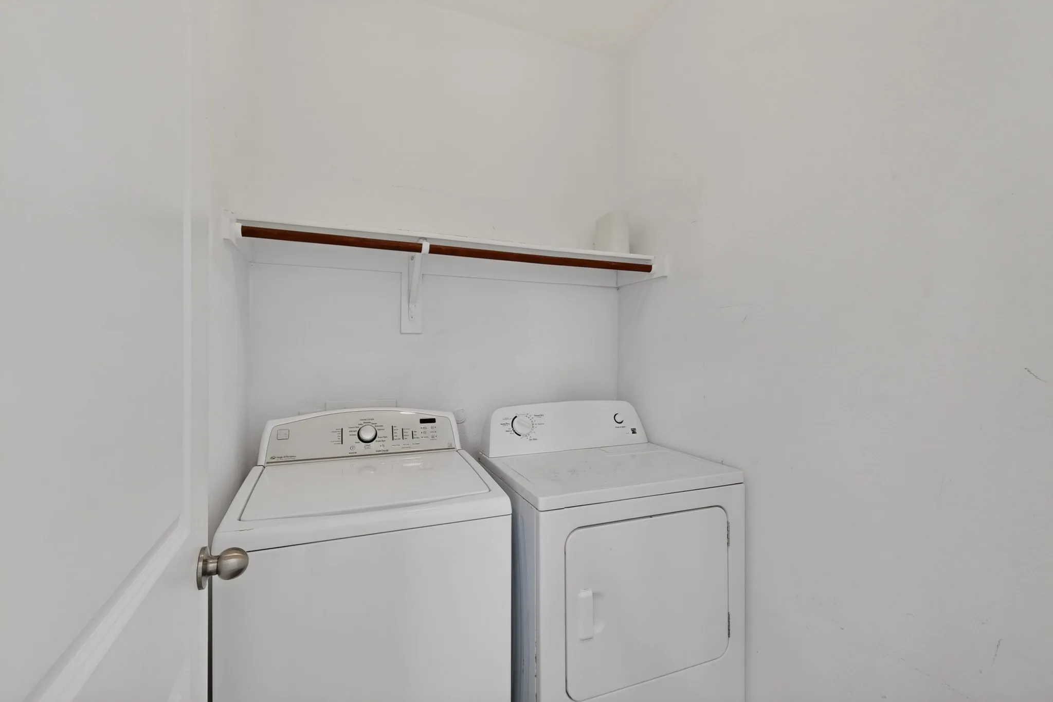 Dedicated laundry area featuring a white top-load washing machine, a white front-load dryer, and an overhead storage shelf