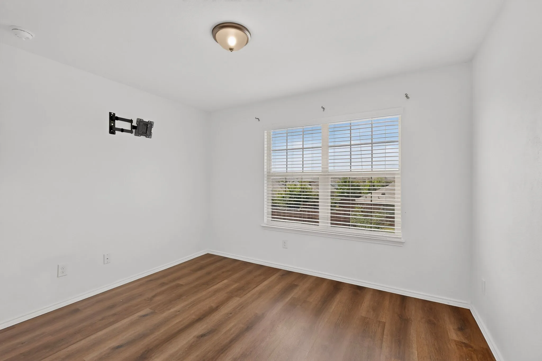 Bright room featuring wood-finish flooring, white baseboards, a large window with white blinds, and a ceiling-mounted light fixture