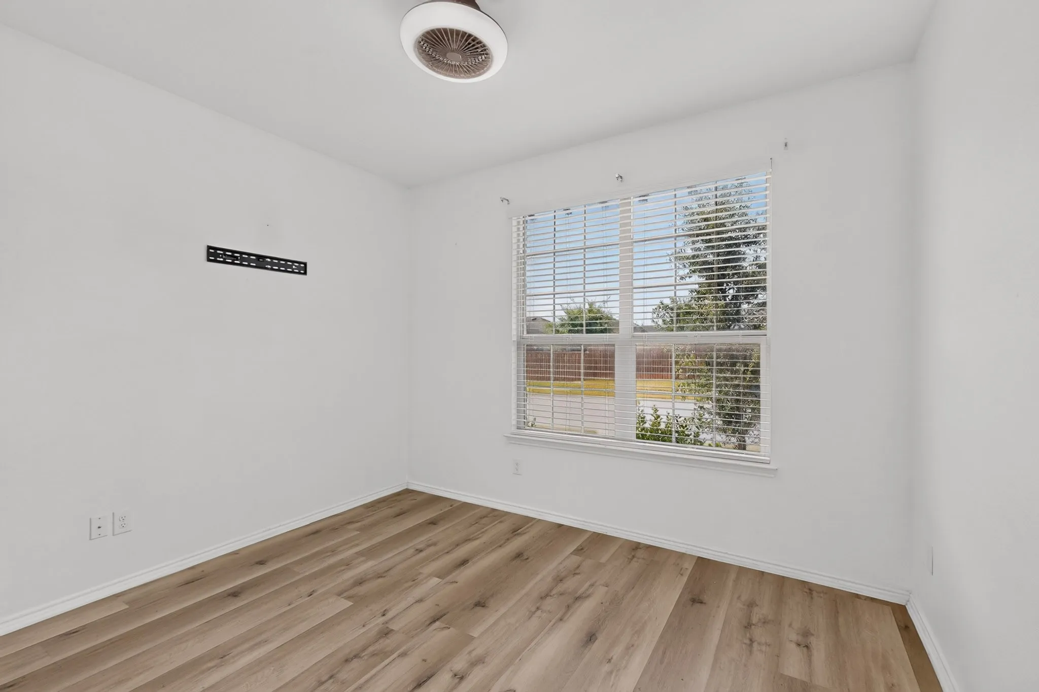 Room featuring wood-finish flooring, a double-hung window with blinds, and a ceiling-mounted light fixture