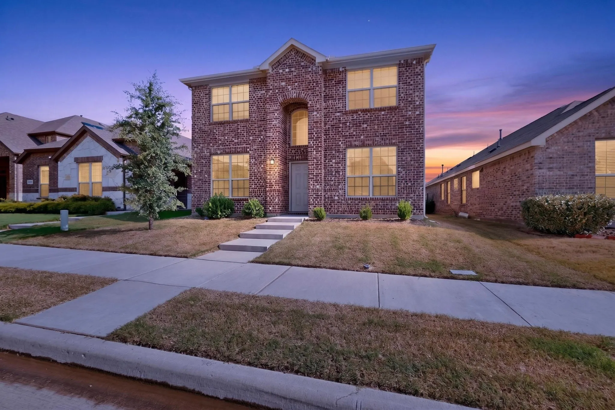 Two-story brick facade residence featuring multiple windows, a prominent arched entry, and a concrete walkway leading to the front door