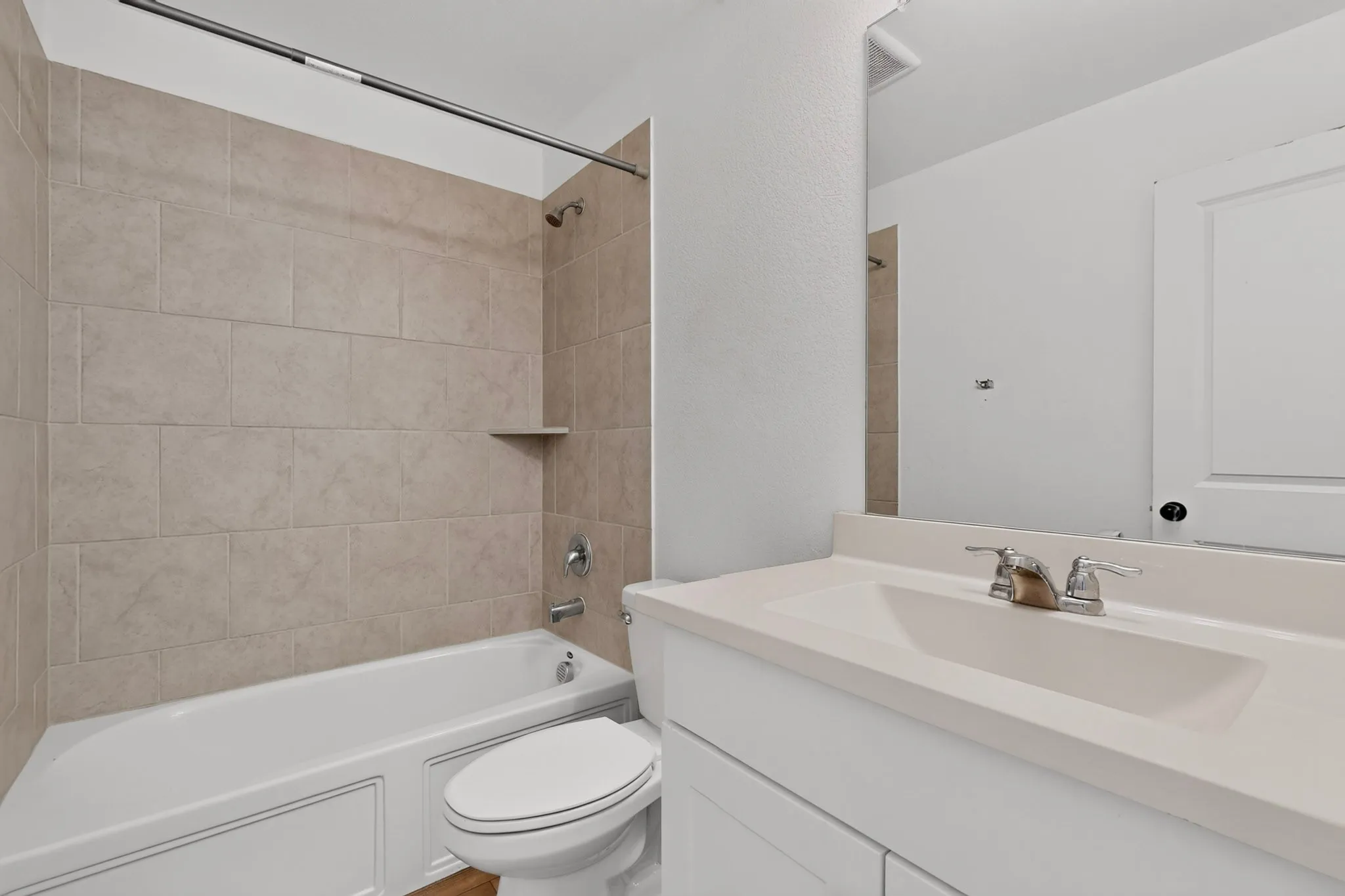 Bathroom featuring a tub/shower combination with large format beige wall tiling and a built-in corner shelf