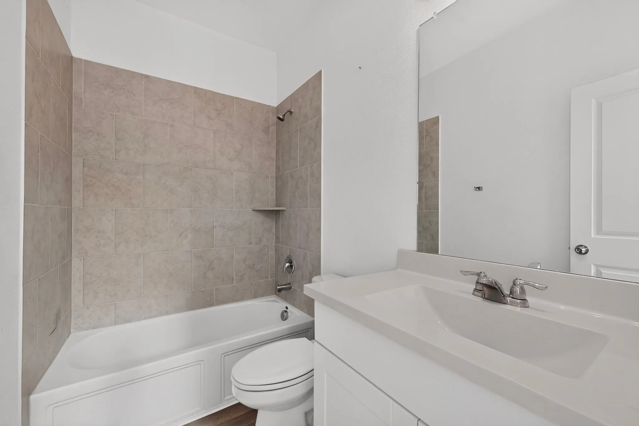 Full bathroom featuring a single white vanity with an integrated sink and chrome faucet, a large frameless mirror, a built-in tub with a shower, and light-toned wall tiling