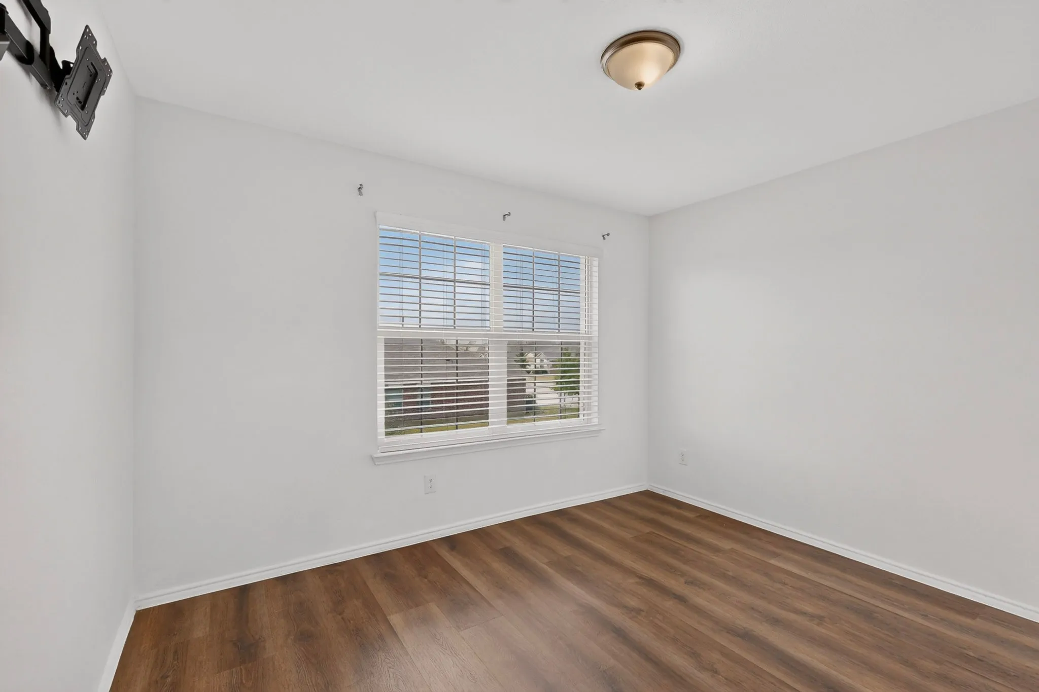 Room featuring wood-finish flooring, white baseboards, and a window with blinds