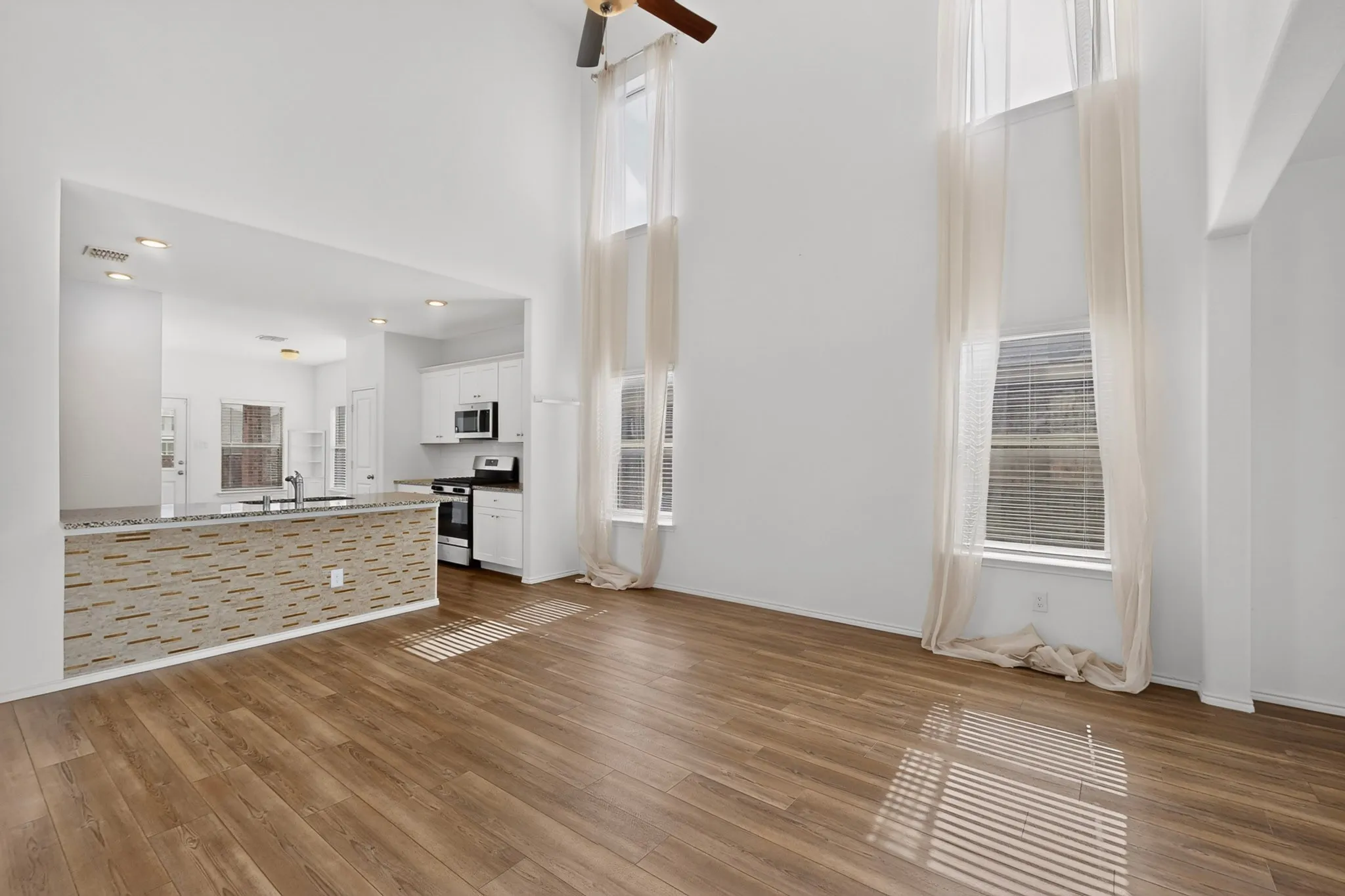 Soaring ceilings featuring tall windows, wood-finish flooring, and a contemporary ceiling fan
