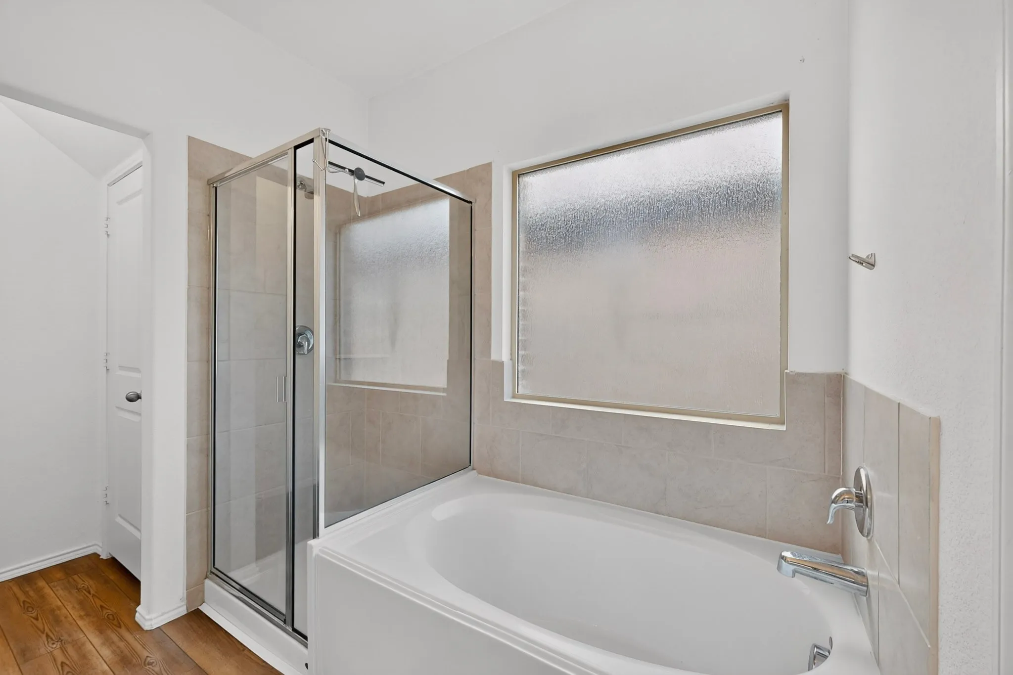 Bathroom featuring a built-in tub, separate glass-enclosed shower, wall-mounted window, and polished chrome fixtures