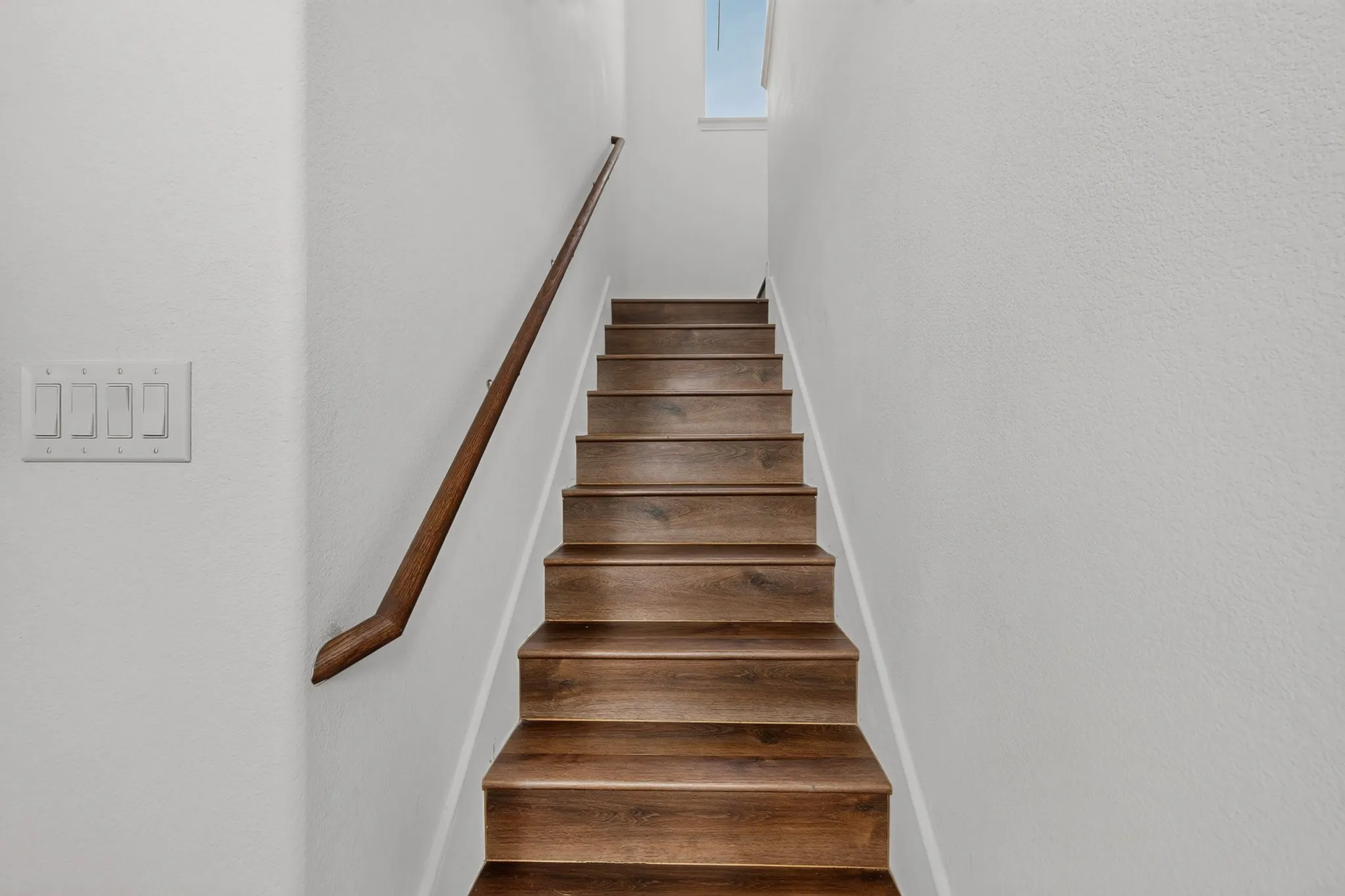 Staircase featuring wood-finish treads and a dark wood handrail, complemented by light neutral wall finishes