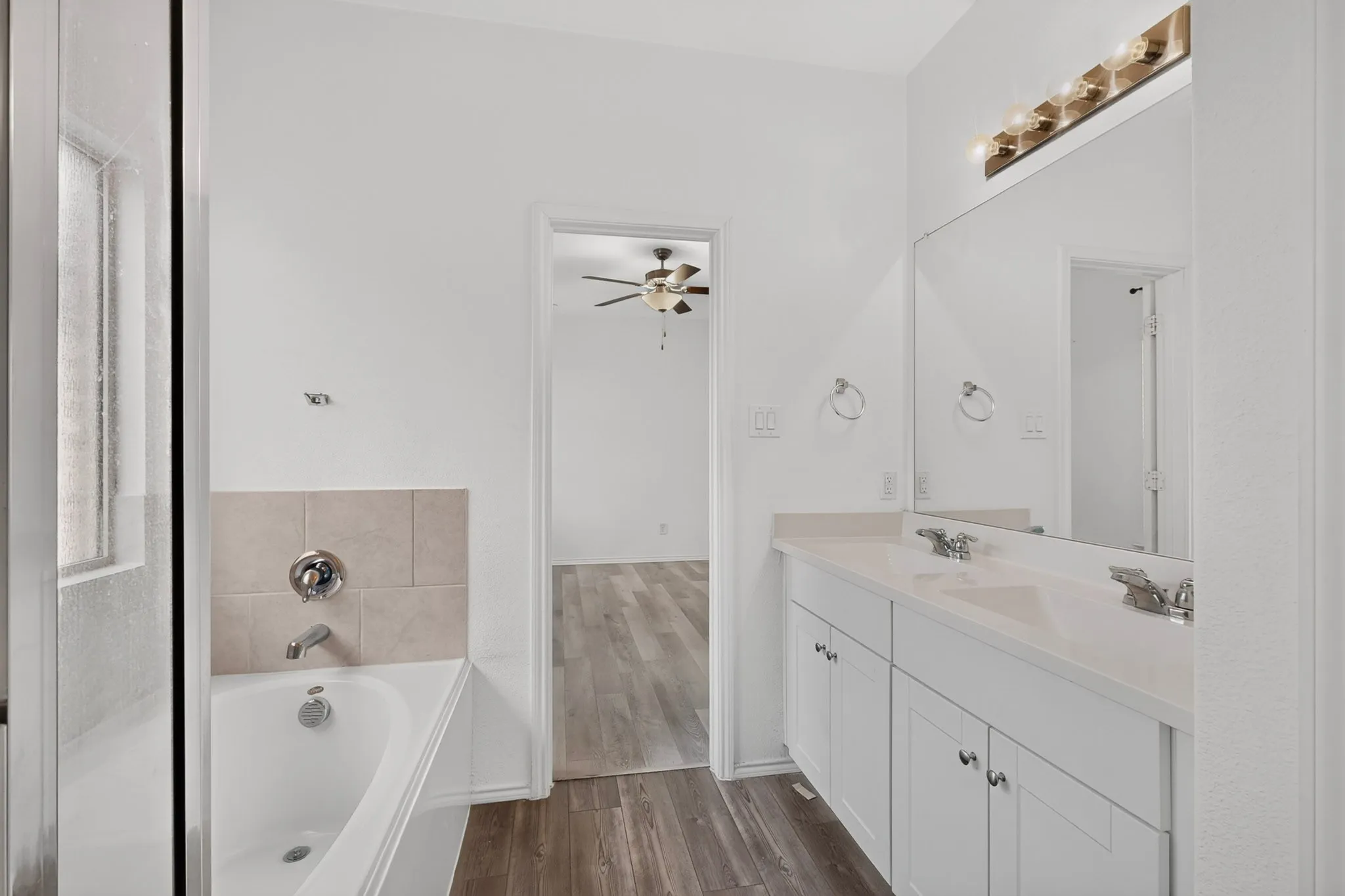 Dual vanity with white cabinetry, a large integrated mirror, and a multi-bulb light fixture