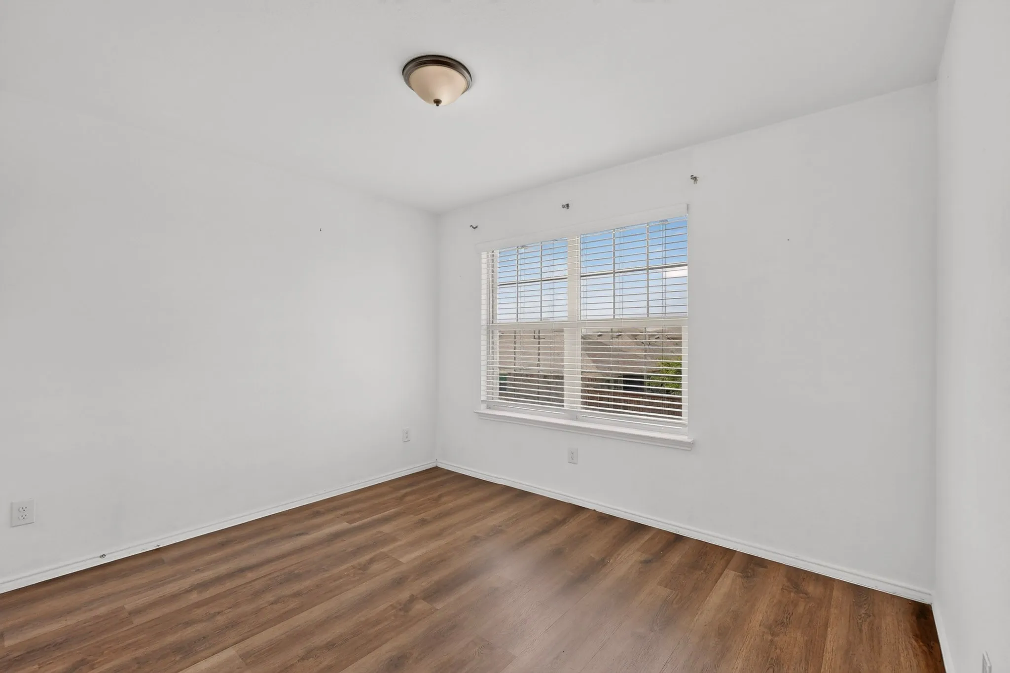 Room featuring wood-finish flooring, white baseboards, and a window with horizontal blinds