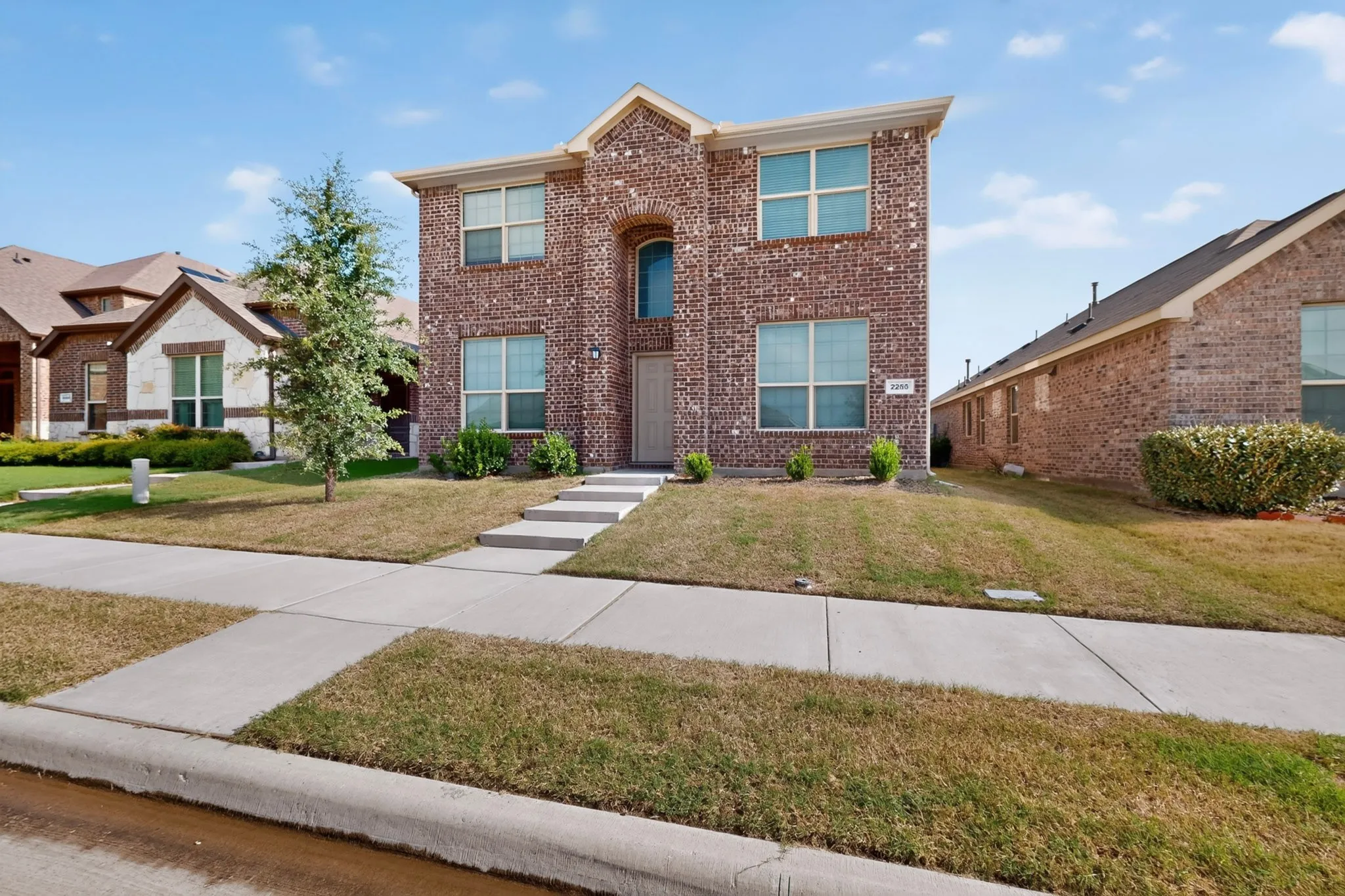 Two-story brick facade residence featuring multiple windows, a prominent arched entry, and a concrete walkway