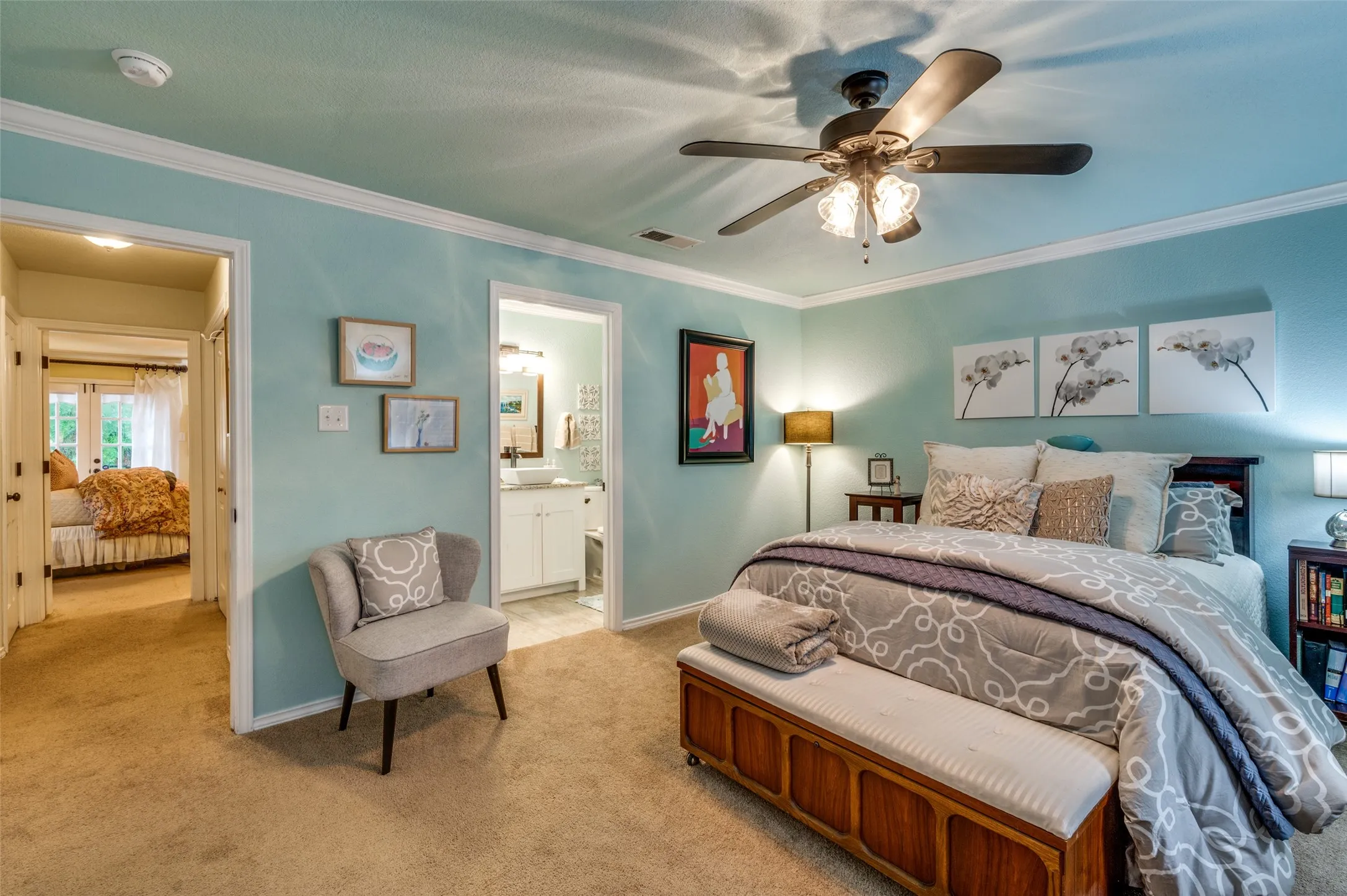 Carpeted bedroom featuring ceiling fan, ornamental molding, and ensuite bath