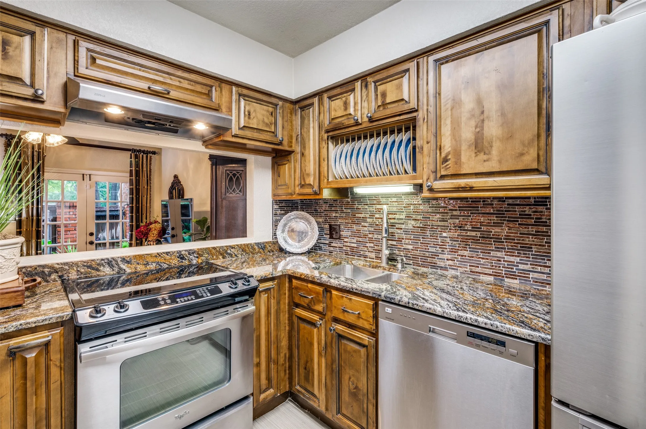Kitchen with stone counters and backsplash, stainless steel appliances, and sink
