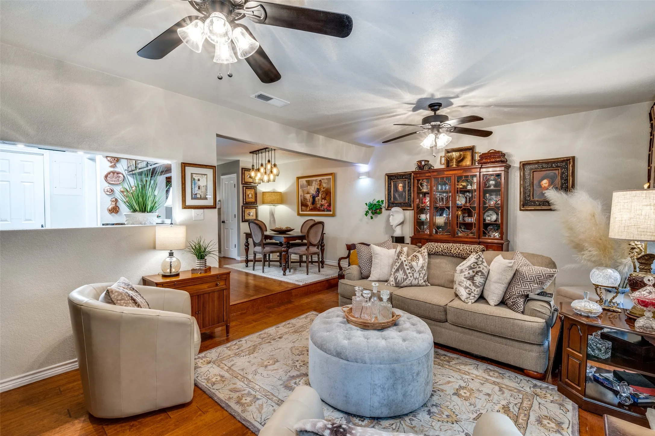 Living room with ceiling fan with notable chandelier and wood-style flooring