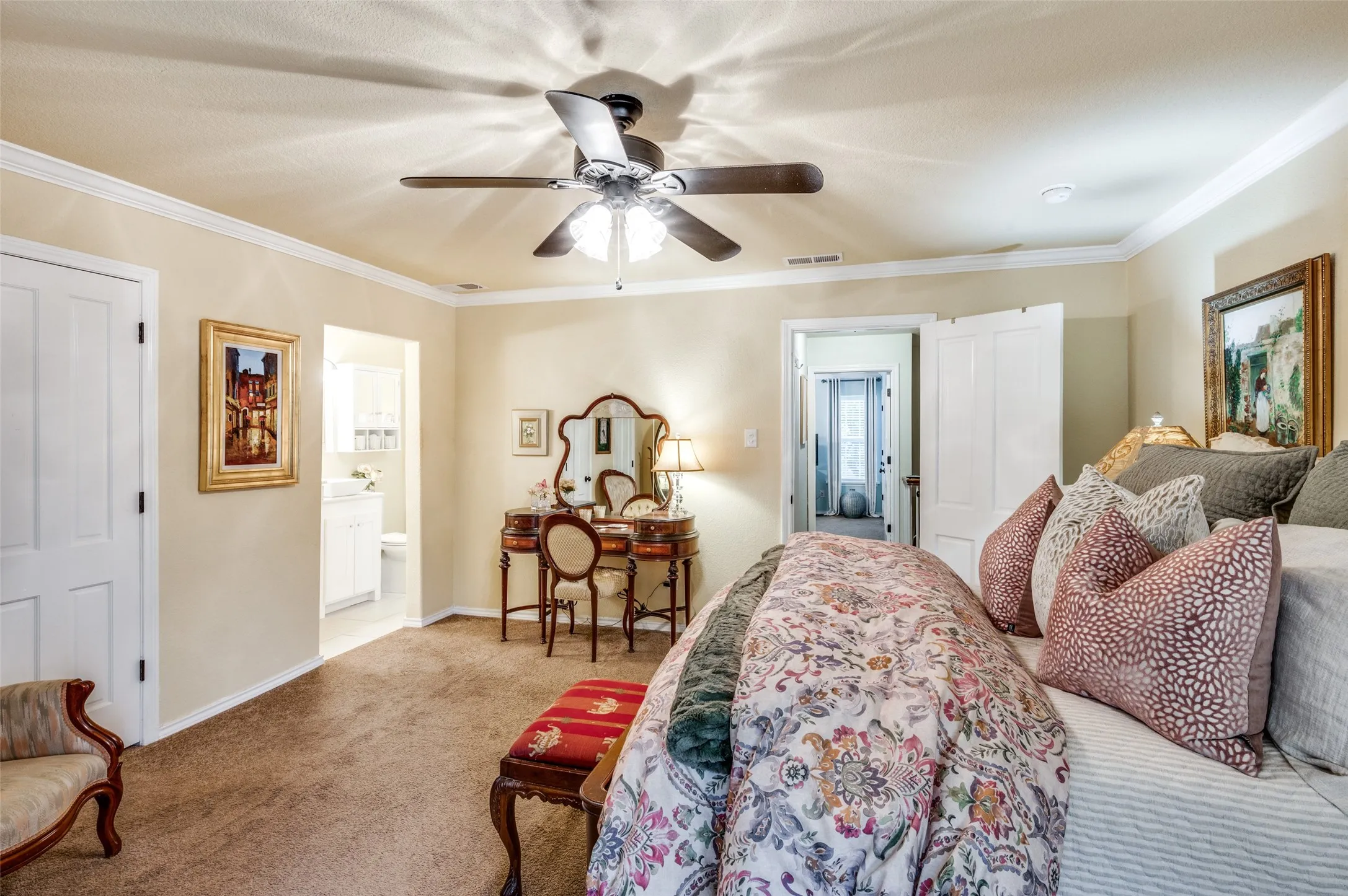 Bedroom featuring ceiling fan, light colored carpet, ornamental molding, and ensuite bath