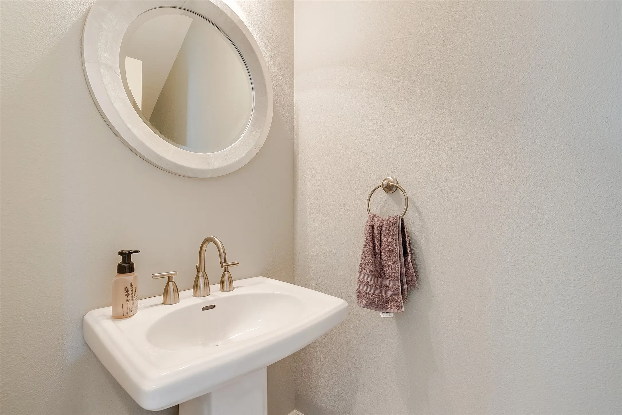 Pedestal sink with brushed nickel faucet, complemented by a circular framed mirror and towel ring