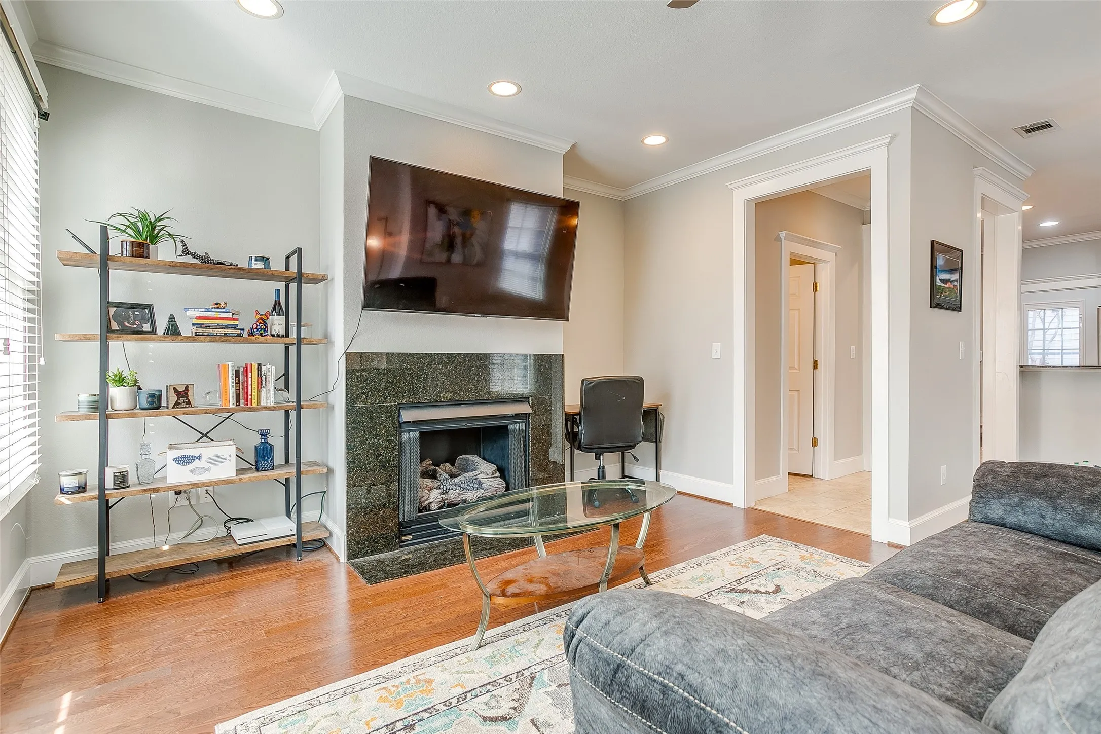 Living area featuring a fireplace with a dark stone surround, wood-finish flooring, recessed lighting, crown molding, and bright white trim