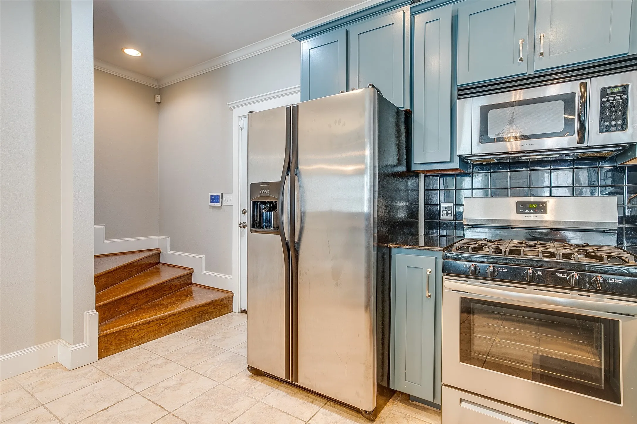 Kitchen featuring slate blue cabinetry, black subway tile backsplash, stainless steel appliances, and a gas range