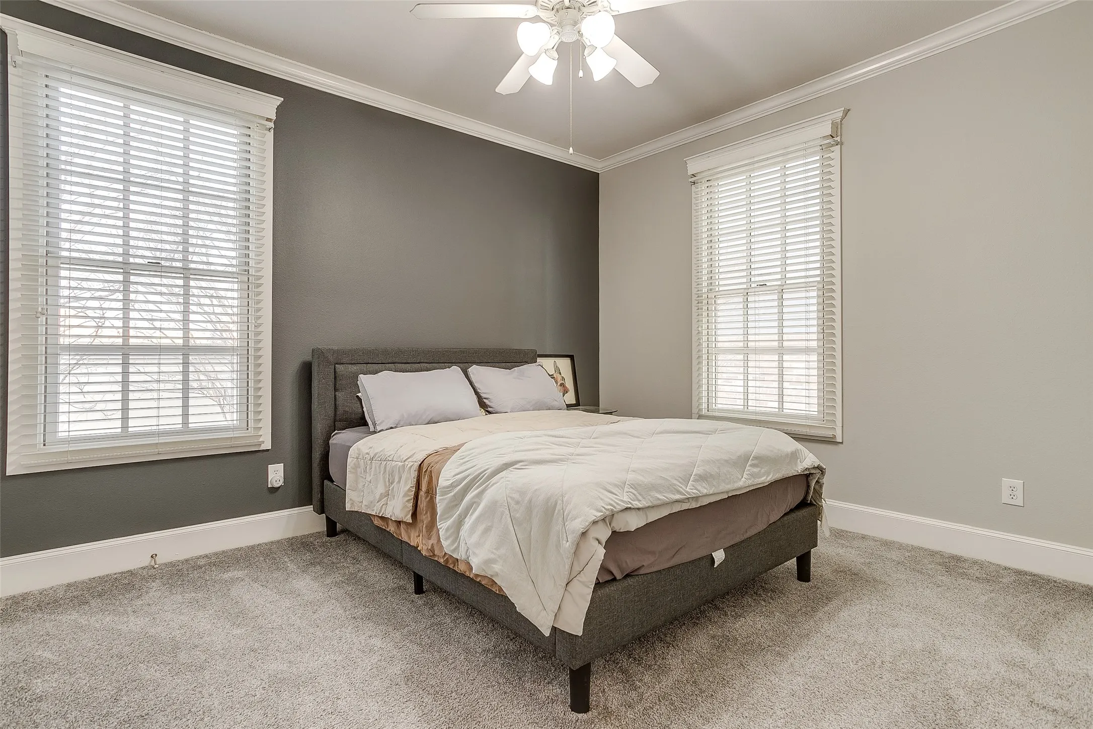 Bedroom featuring gray wall accent, light gray walls, white crown molding, white baseboards, and light gray carpeting