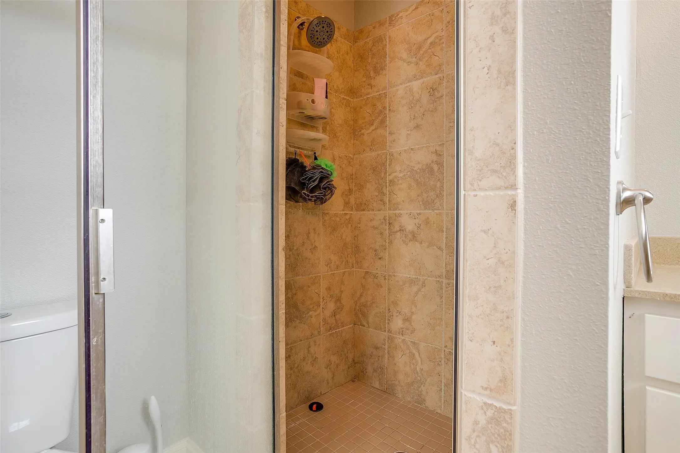 Walk-in shower featuring natural-toned tile surround and a coordinating tiled floor