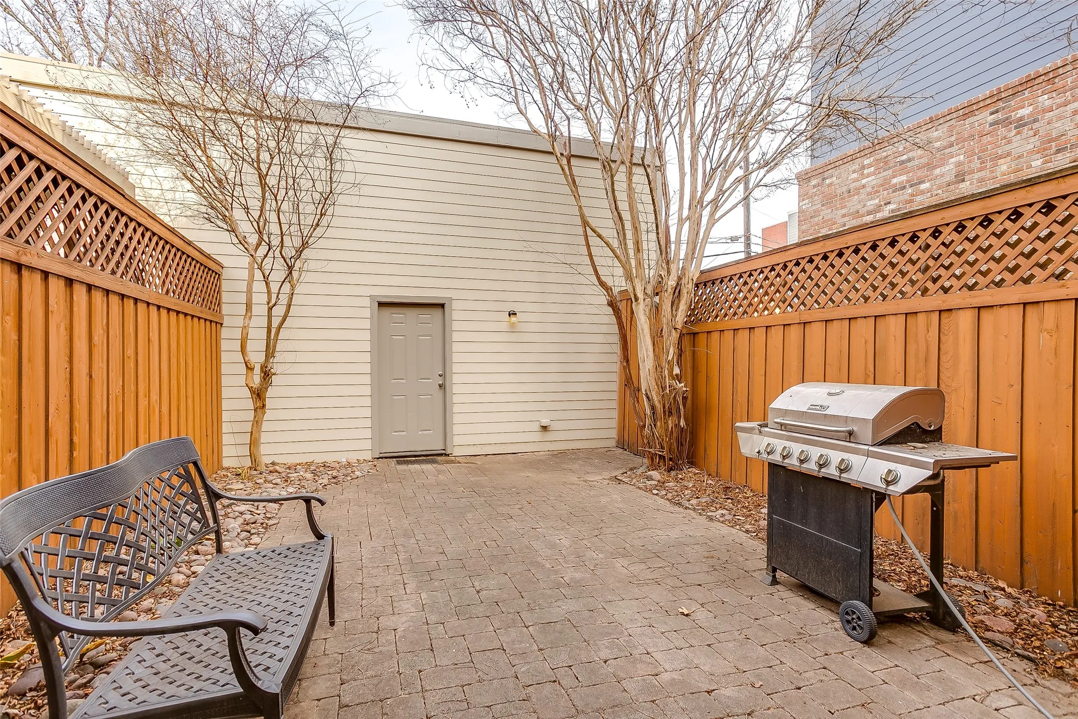 Private paver patio featuring a full-height wooden fence with lattice detailing, a separate exterior door, and a gravel border