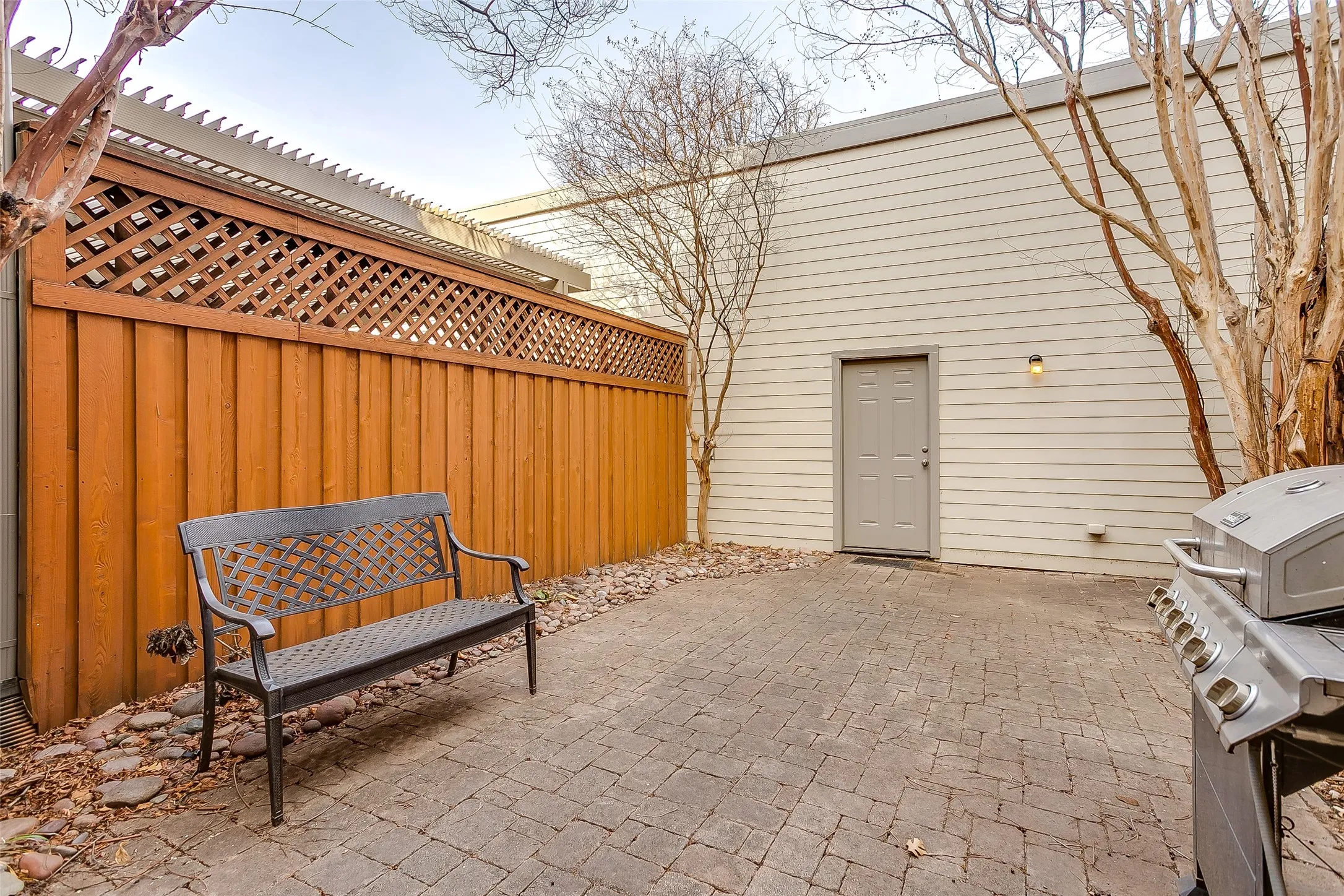 Paved patio featuring a wood privacy fence with lattice top, tan siding, and an exterior door