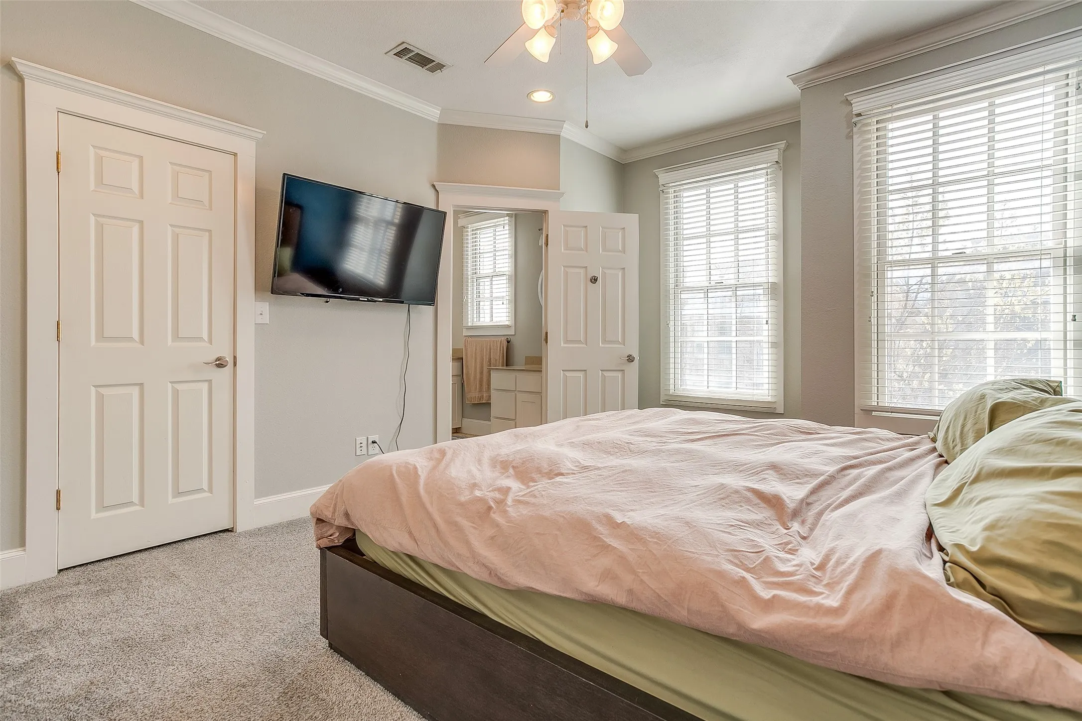 Carpeted room featuring two prominent windows with blinds, a ceiling fan with integrated lighting, and a six-panel interior door