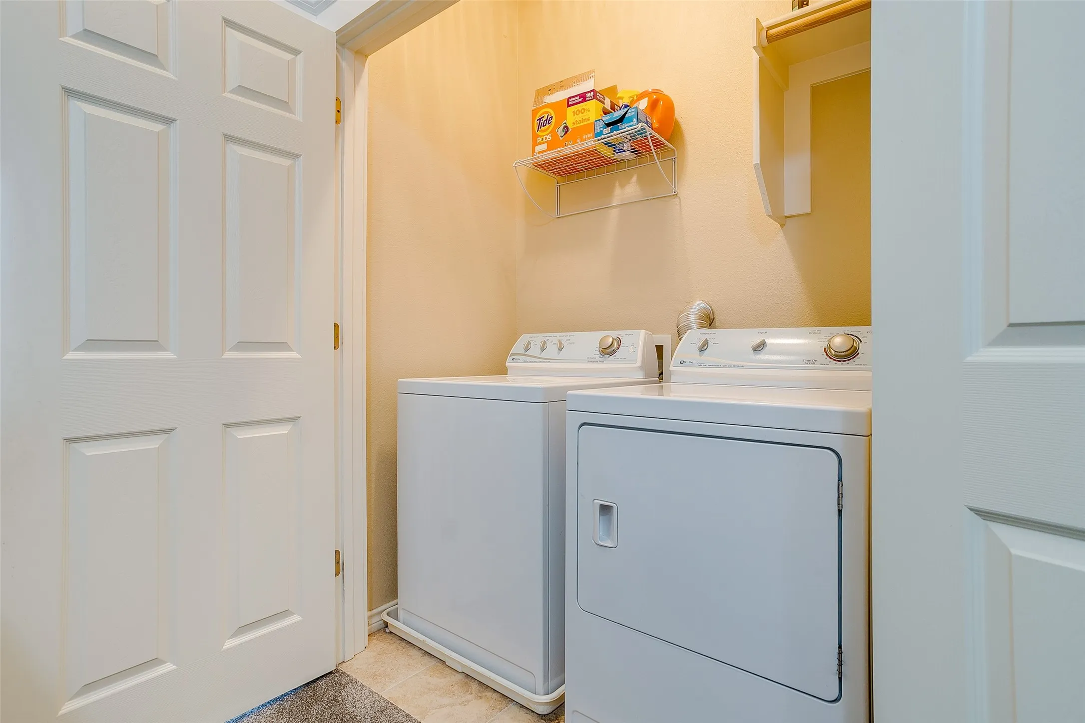 Dedicated laundry area featuring a tile floor, wall-mounted shelving, and a six-panel interior door