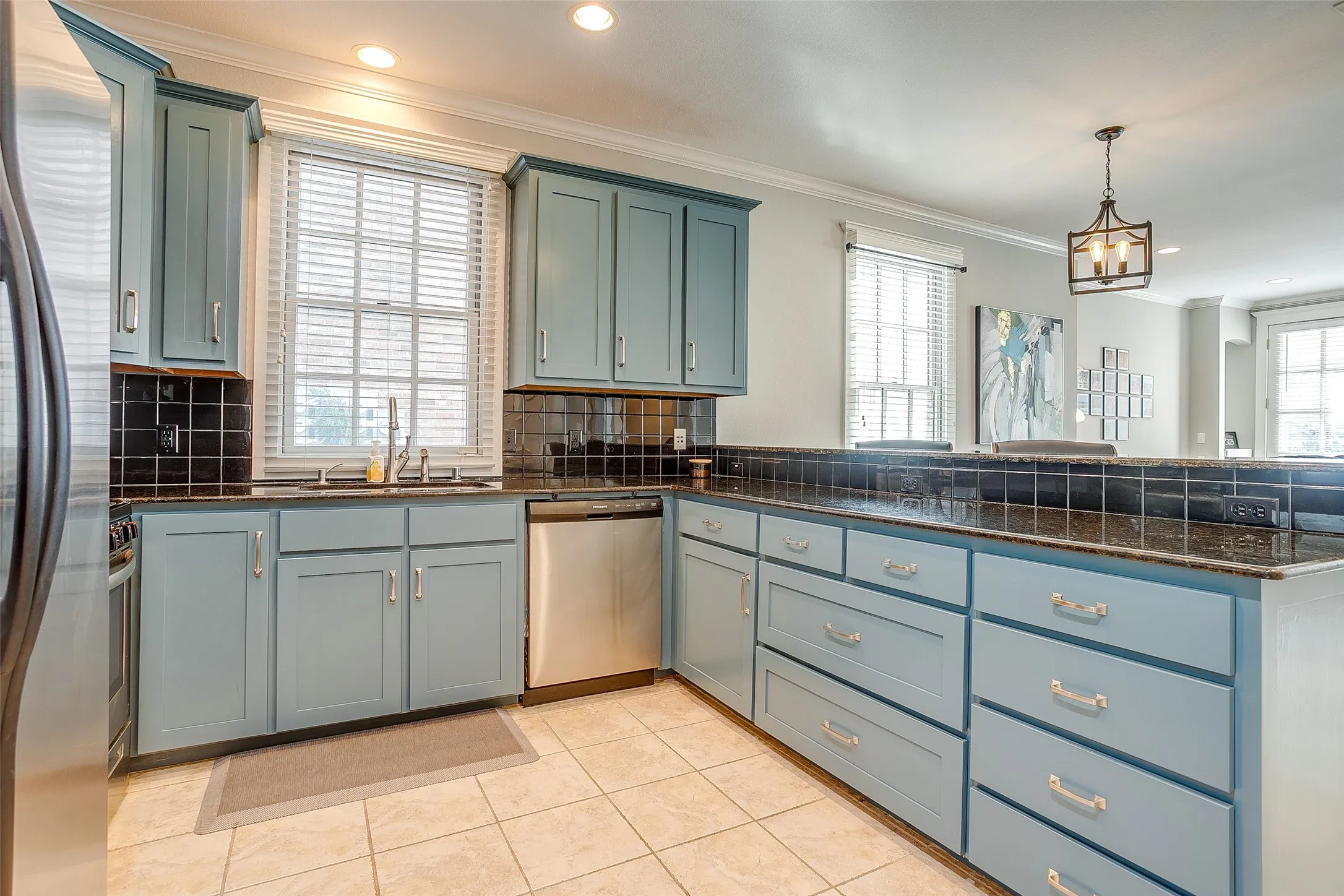 Kitchen featuring light blue cabinetry with brushed nickel hardware, black tile backsplash, and dark speckled countertops