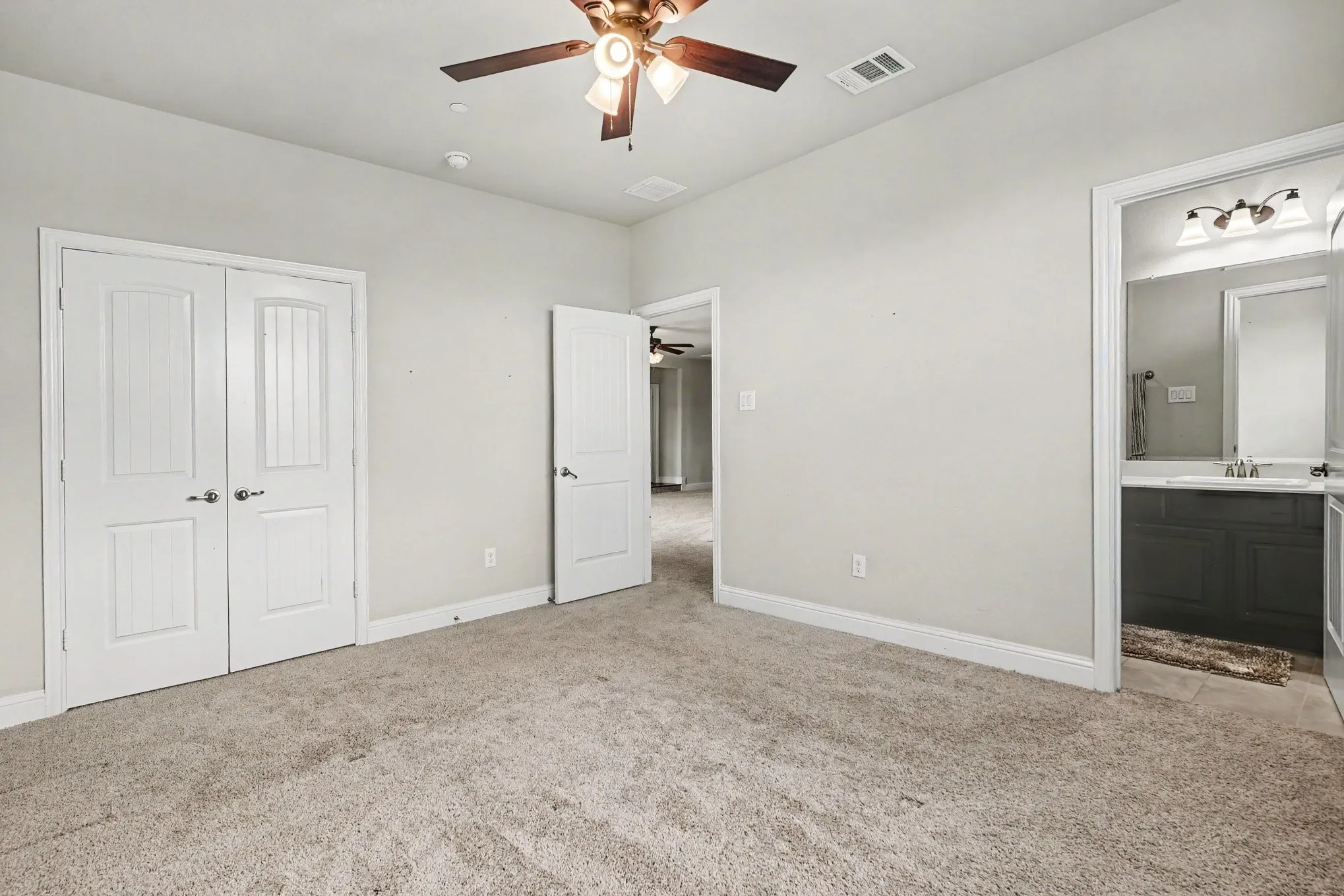 Front Bedroom with EnSuite Bathroom featuring carpeted room, a ceiling fan, white paneled doors, and direct access to a bathroom with a vanity and mirror