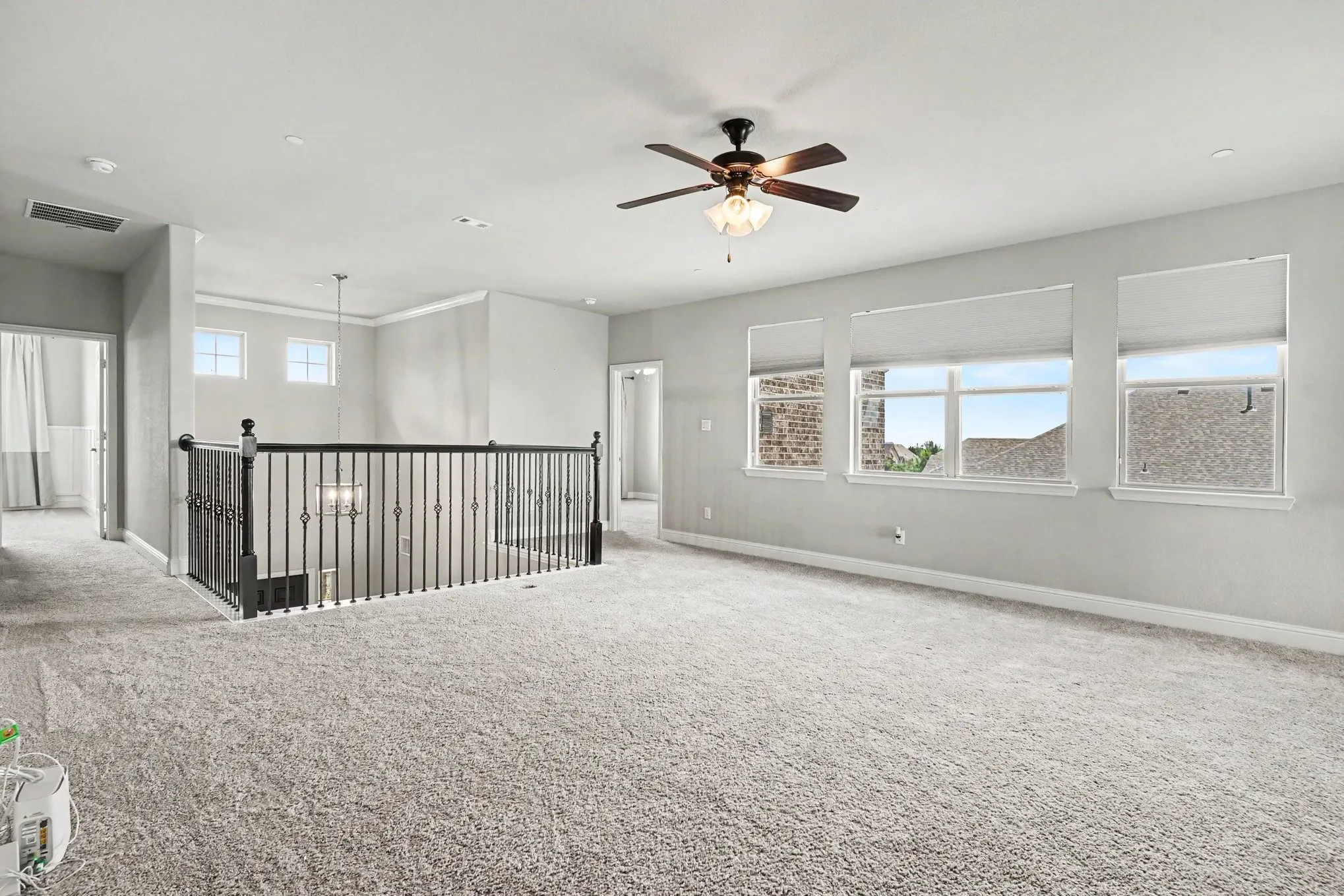 2nd Floor Living Area featuring a carpeted room, multiple windows with roller shades, a ceiling fan with integrated lighting, and a wrought iron balustrade overlooking a lower level