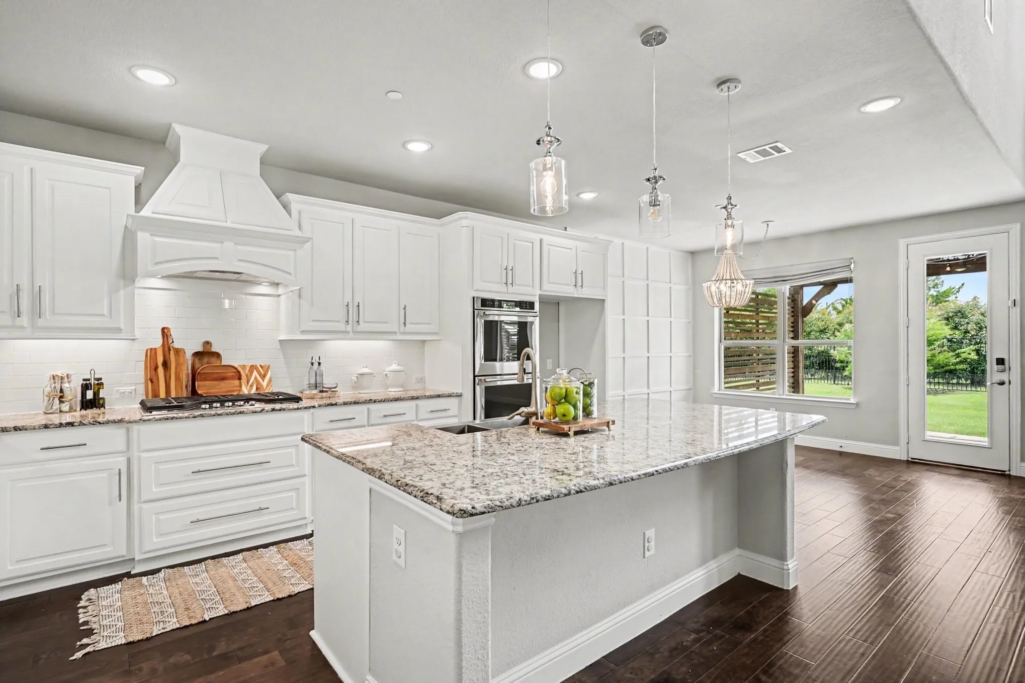 Gourmet kitchen featuring a large island with a stone countertop, white shaker cabinetry, stainless steel double ovens, and wood-finish flooring