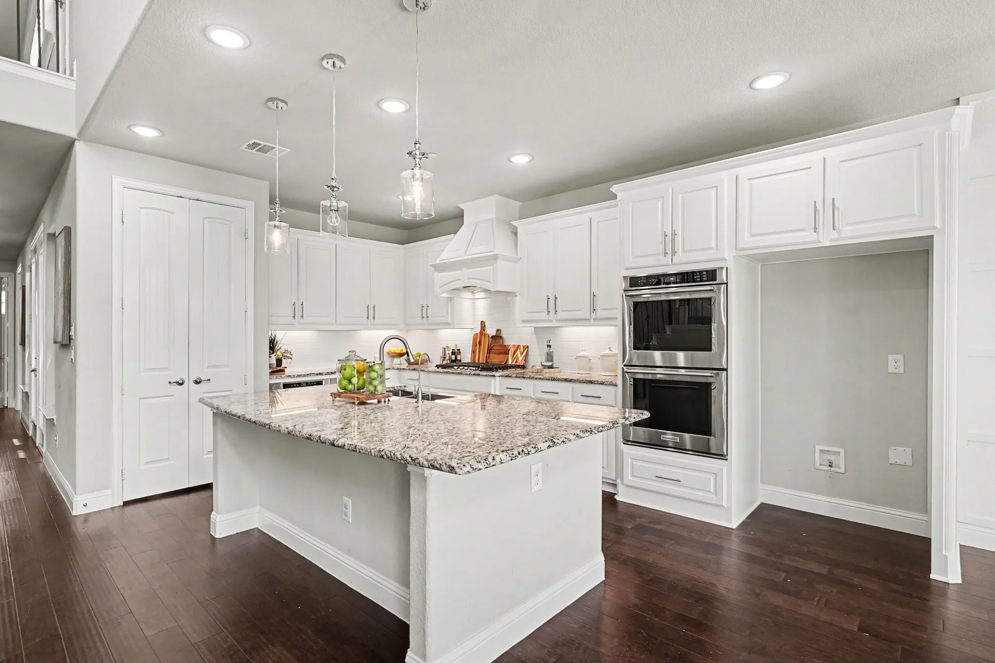 Gourmet kitchen featuring white cabinetry, a granite-topped island with a sink, recessed lighting, and stainless steel double ovens