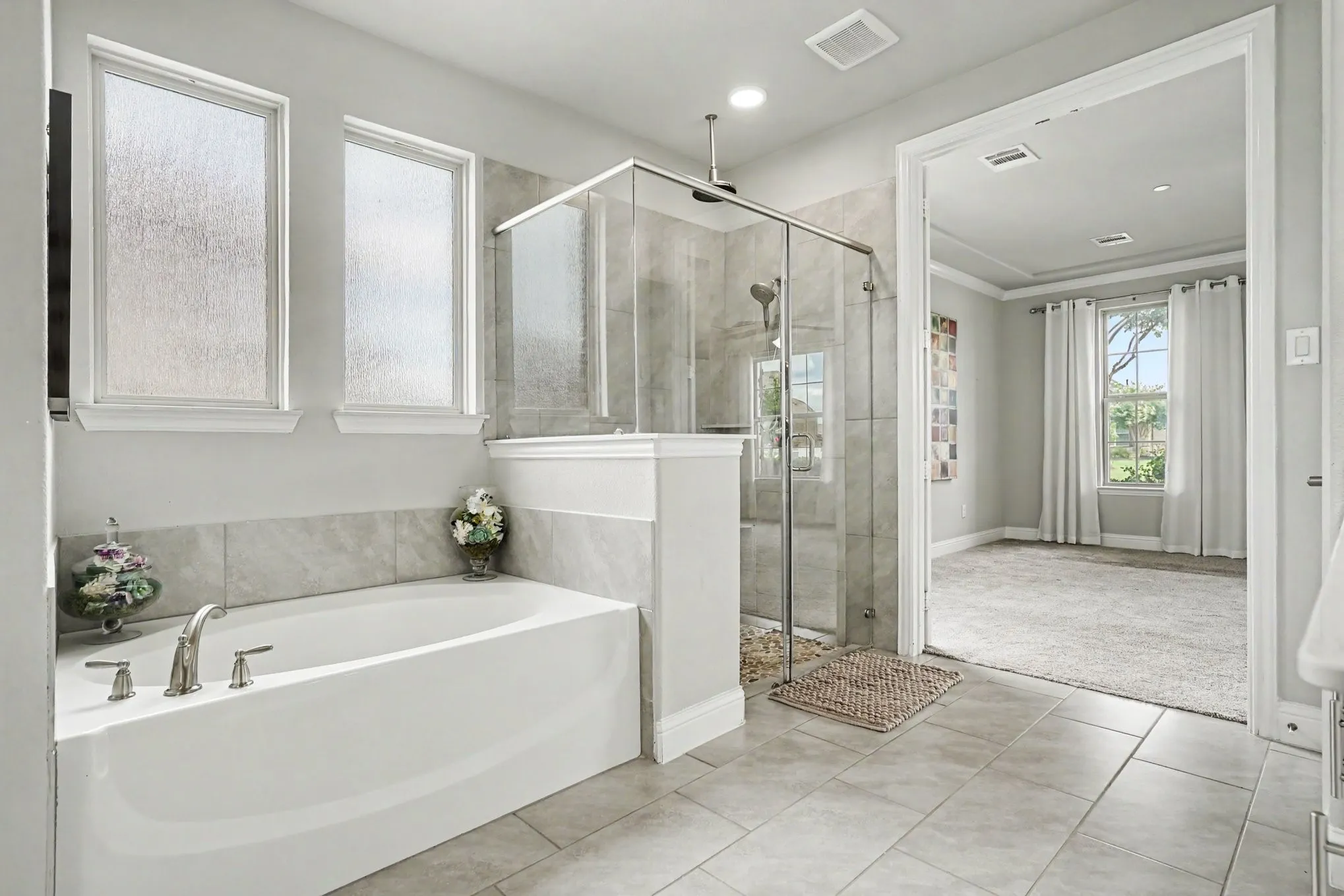 1st Floor Primary Bathroom featuring a built-in soaking tub with deck-mounted fixtures, a glass-enclosed shower with tile surround, and light-toned tile flooring