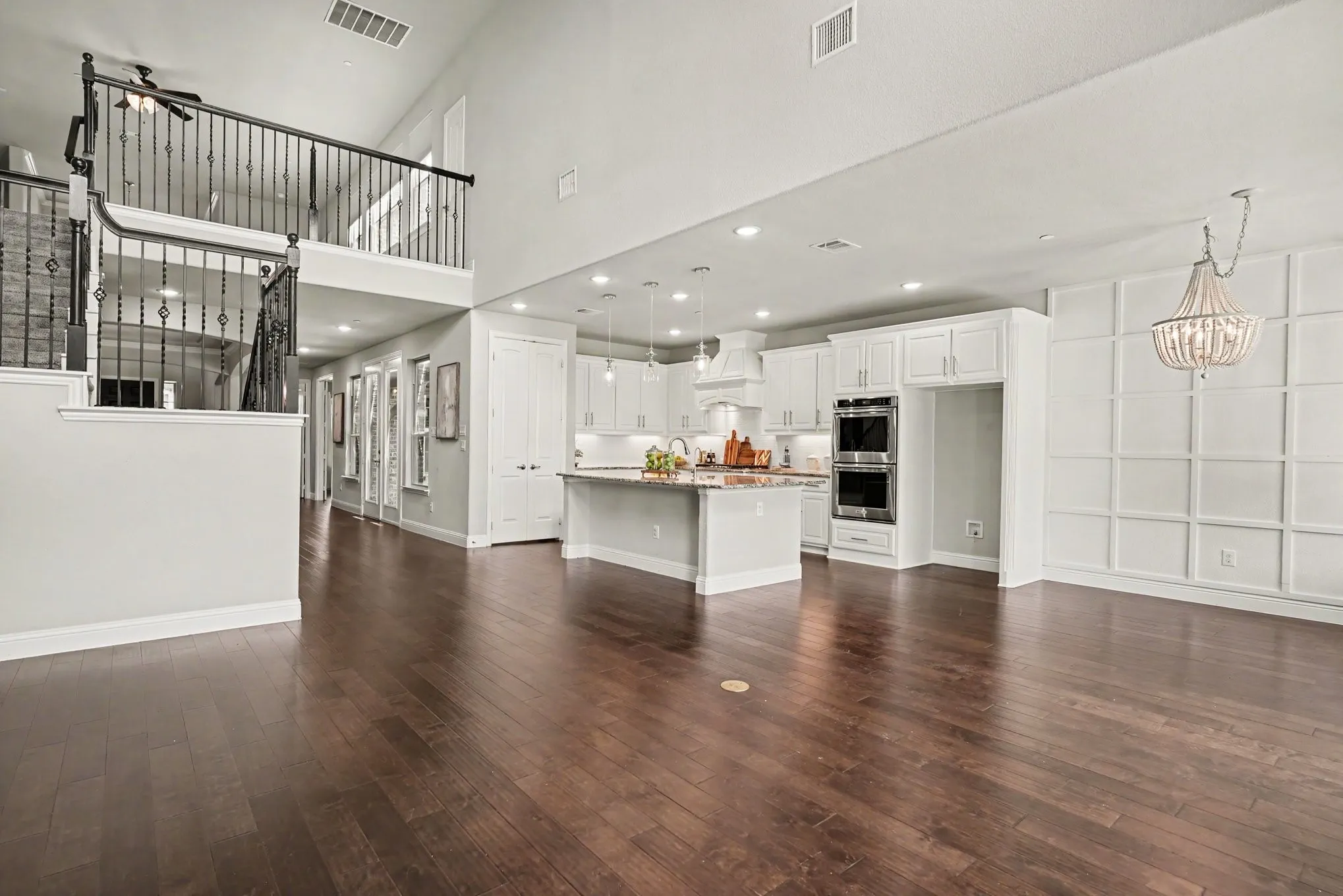 Open-concept living space featuring wood-finish flooring, a contemporary kitchen, a decorative accent wall, and an overhead balcony with iron railings