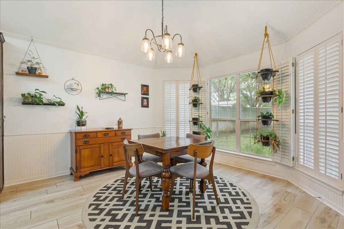 Dining area featuring a bay window with plantation shutters, wood-finish flooring, and wainscoting