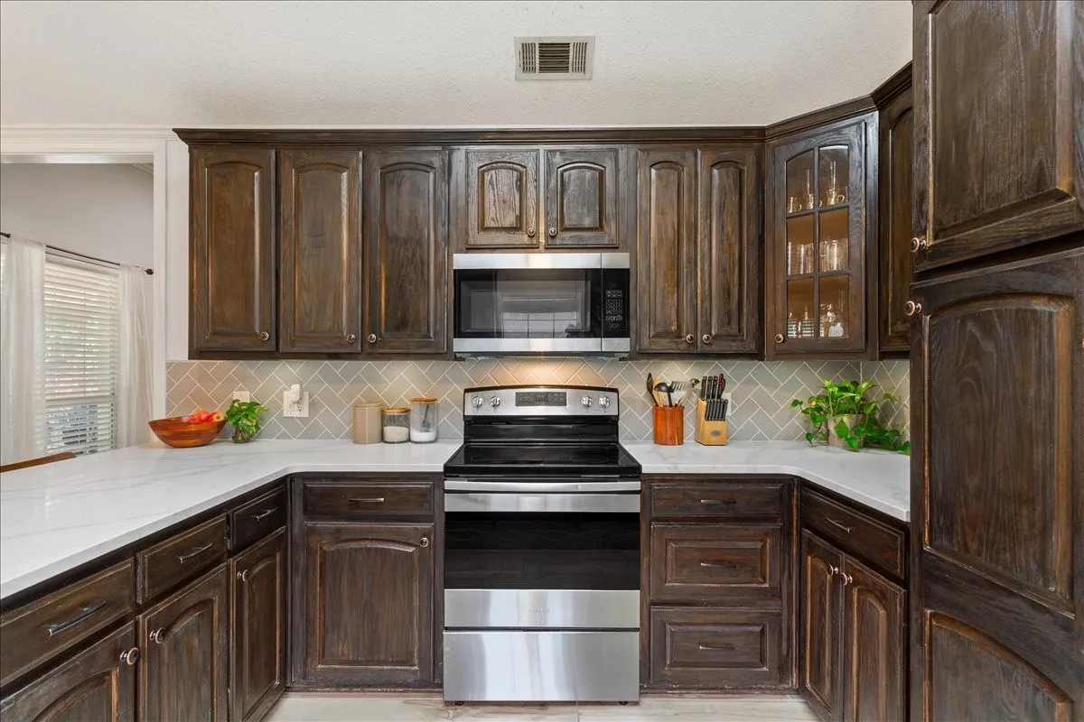 U-shaped kitchen featuring dark wood cabinetry, light-toned countertops, a stainless steel range, and a subway tile backsplash in a herringbone pattern