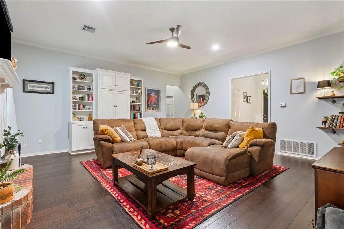 Spacious living area featuring dark wood-finish flooring, built-in white cabinetry, a white crown molding, and recessed lighting