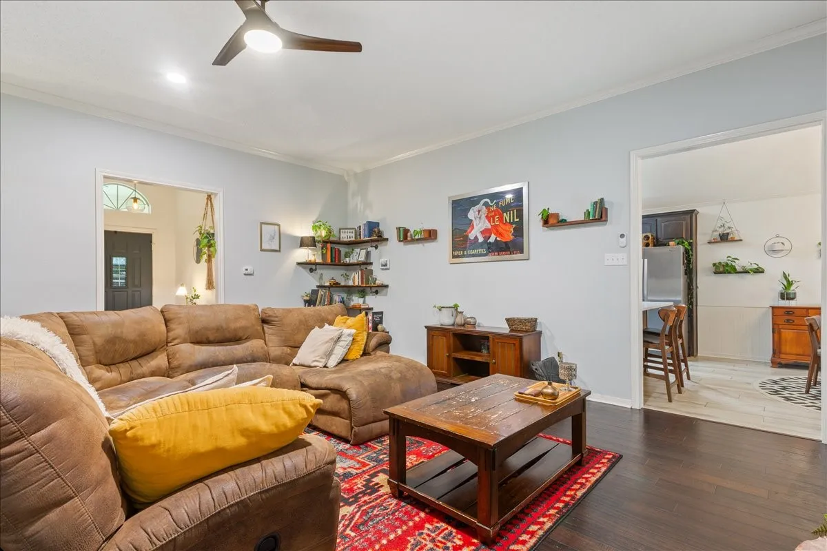 Living area featuring dark wood-finish flooring, light-toned walls, a modern ceiling fan, and open doorways