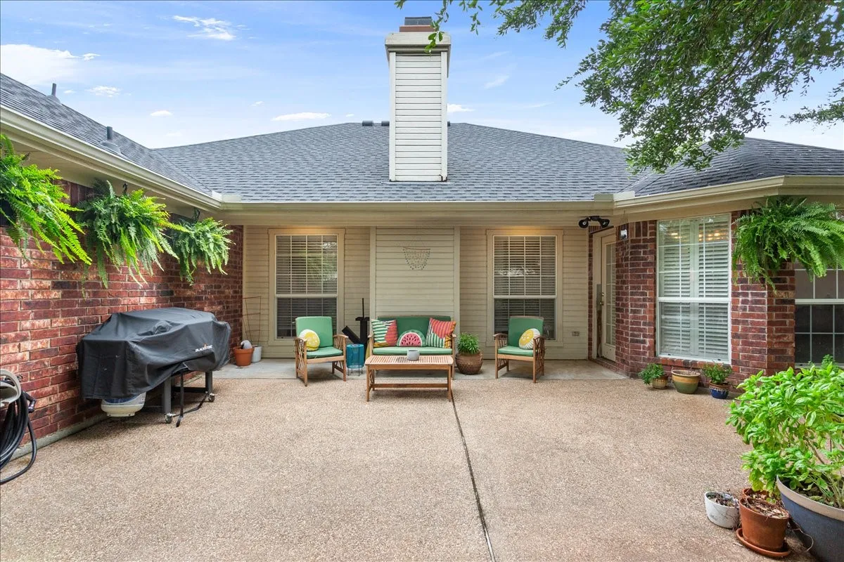 Spacious L-shaped patio with exposed aggregate concrete flooring, brick exterior walls, multiple windows, and a prominent chimney
