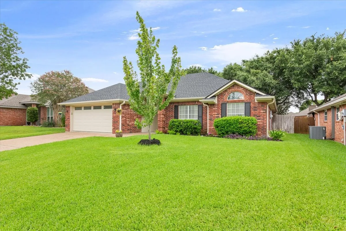 Traditional brick-front residence featuring a two-car garage with a panel door, a dark shingle roof, and a meticulously maintained front lawn