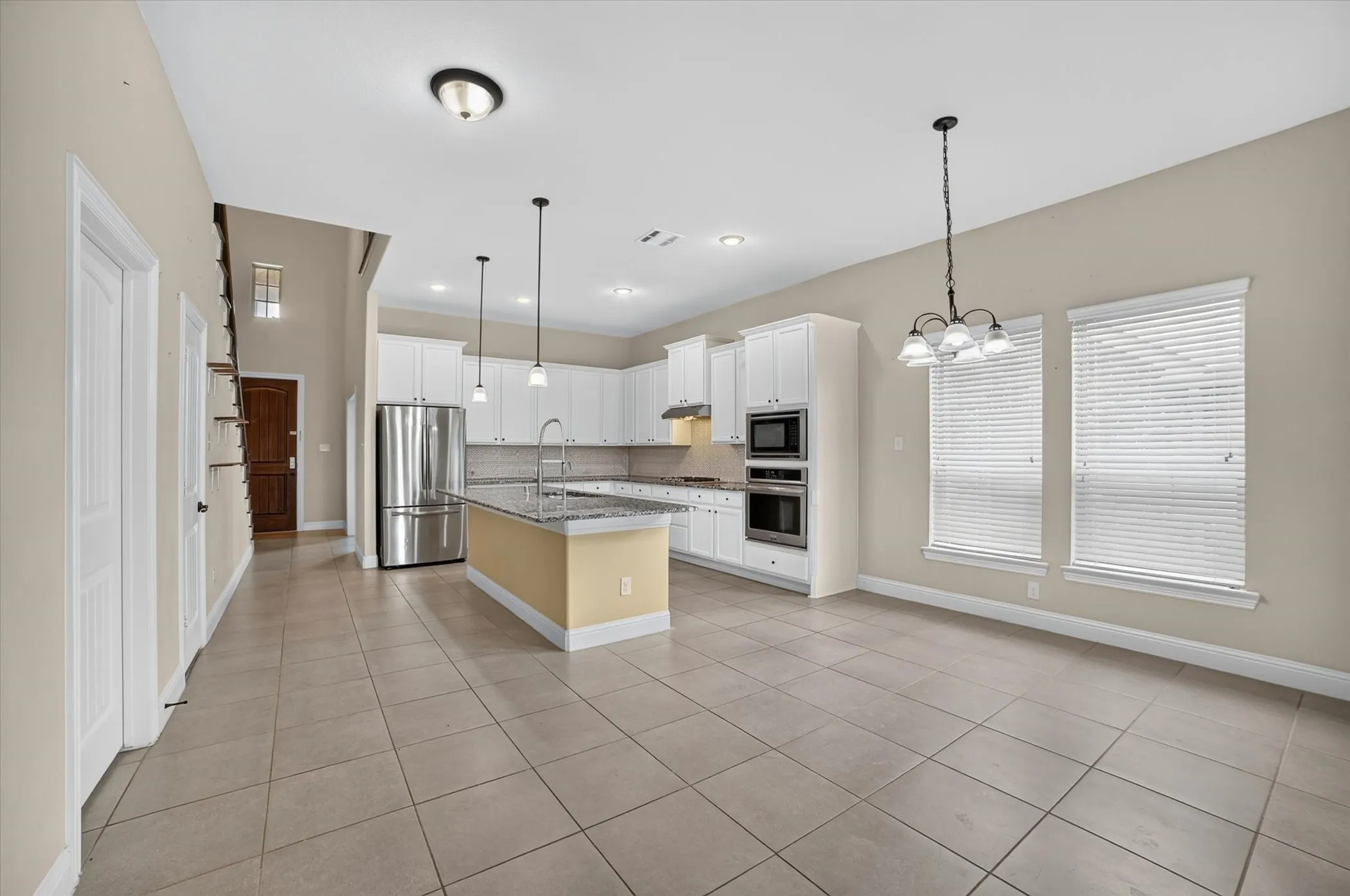 Open-concept living area featuring a kitchen with white cabinetry, stainless steel appliances, a center island with a granite-finish countertop, and tile flooring throughout