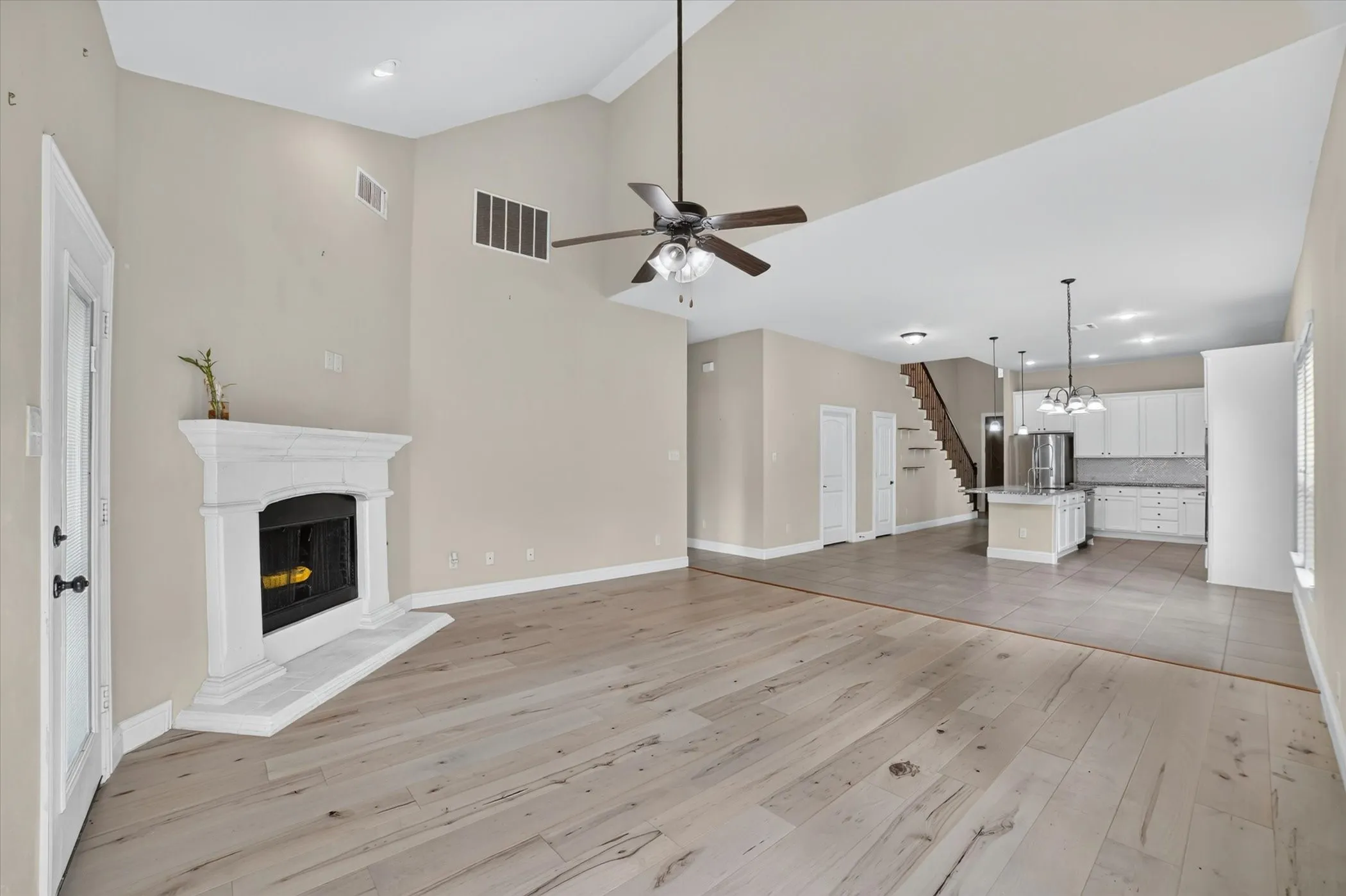 Spacious living area featuring high vaulted ceilings, light wood-finish flooring, and a white mantel fireplace