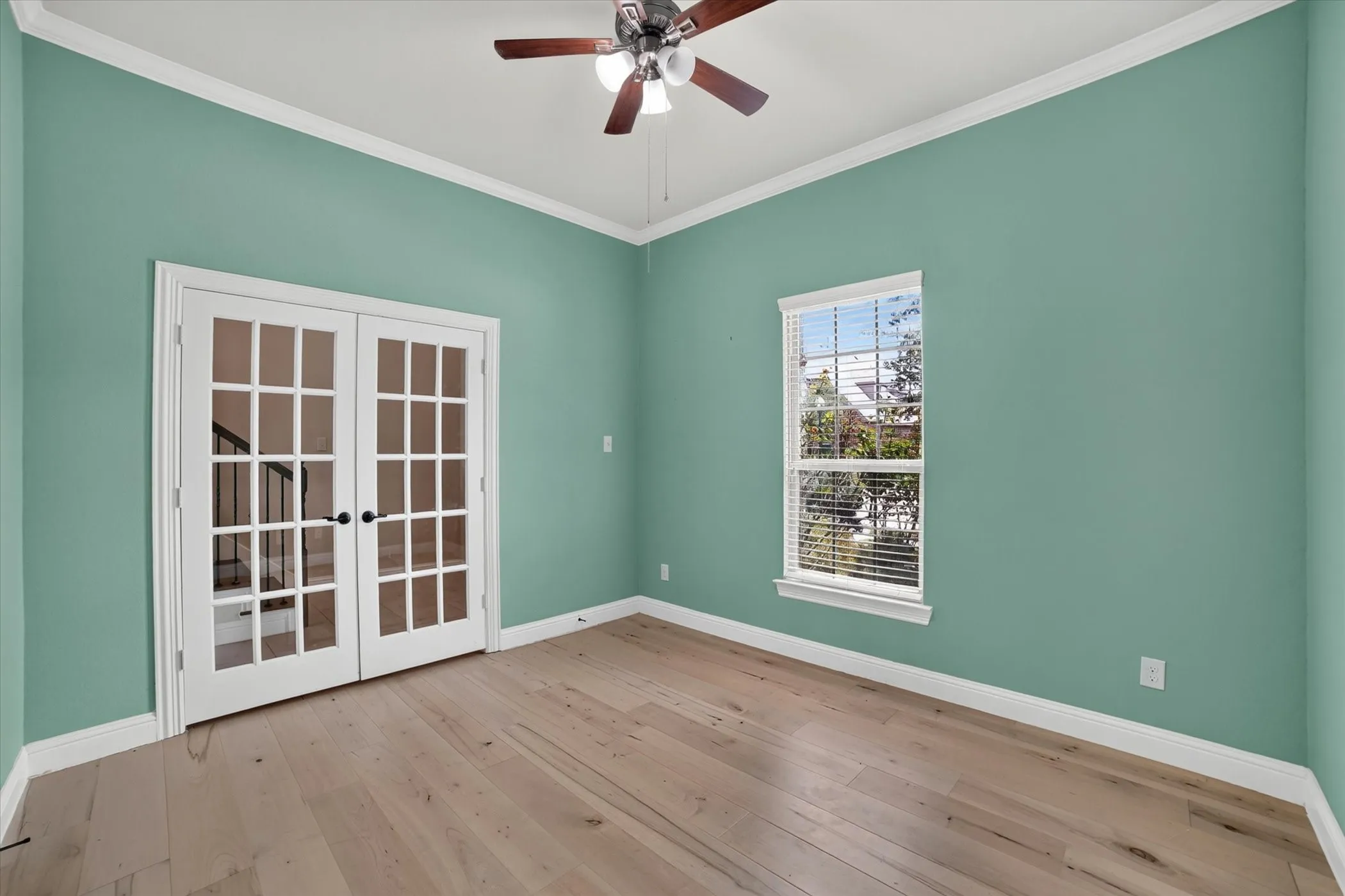 Room featuring light wood-finish flooring, a ceiling fan with light fixture, and a window with blinds