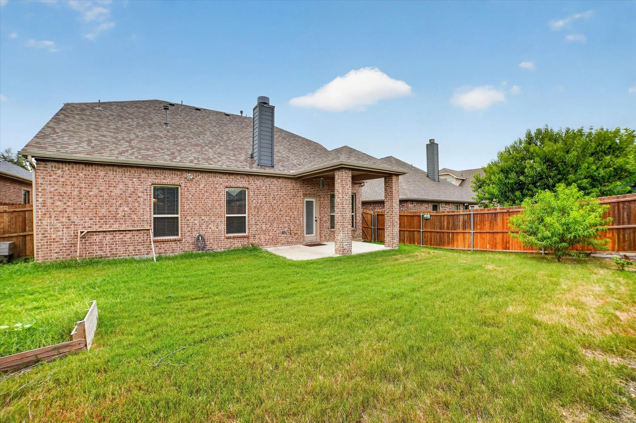 Expansive backyard featuring a covered patio with brick columns, a privacy fence, and a mature tree
