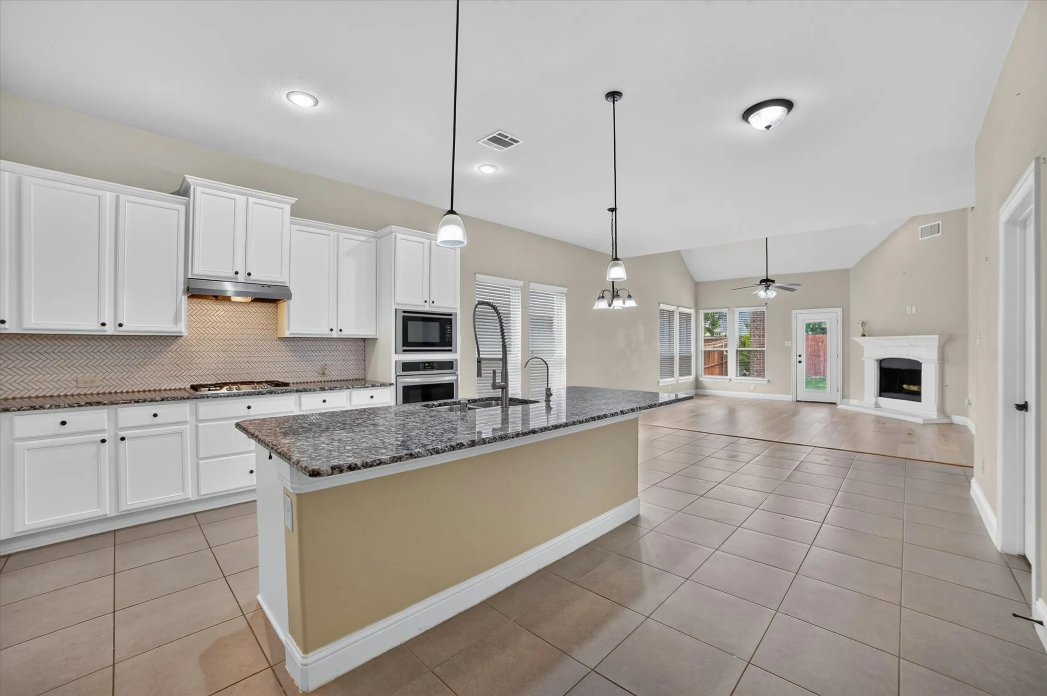 Open-concept kitchen featuring white cabinetry, granite countertops, and a herringbone tile backsplash