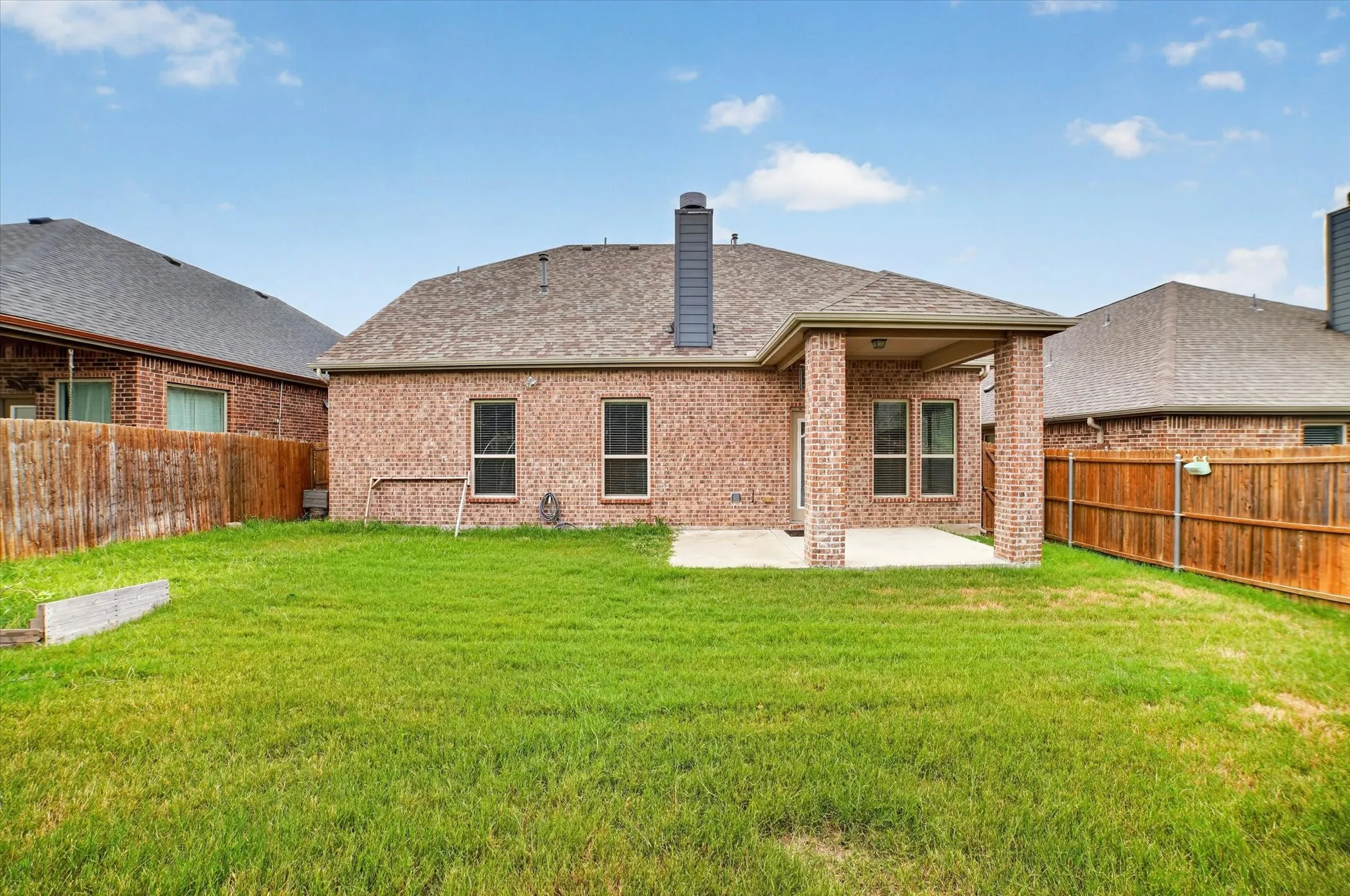 Expansive backyard featuring a covered patio, brick exterior, wood fence, and a pitched roof