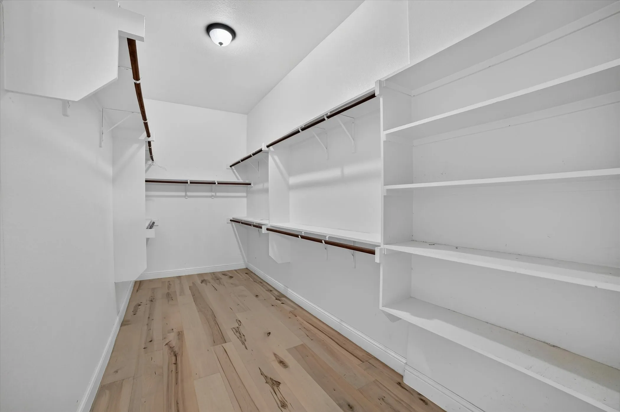 Spacious walk-in closet featuring light wood-finish flooring, white walls, and a recessed ceiling light