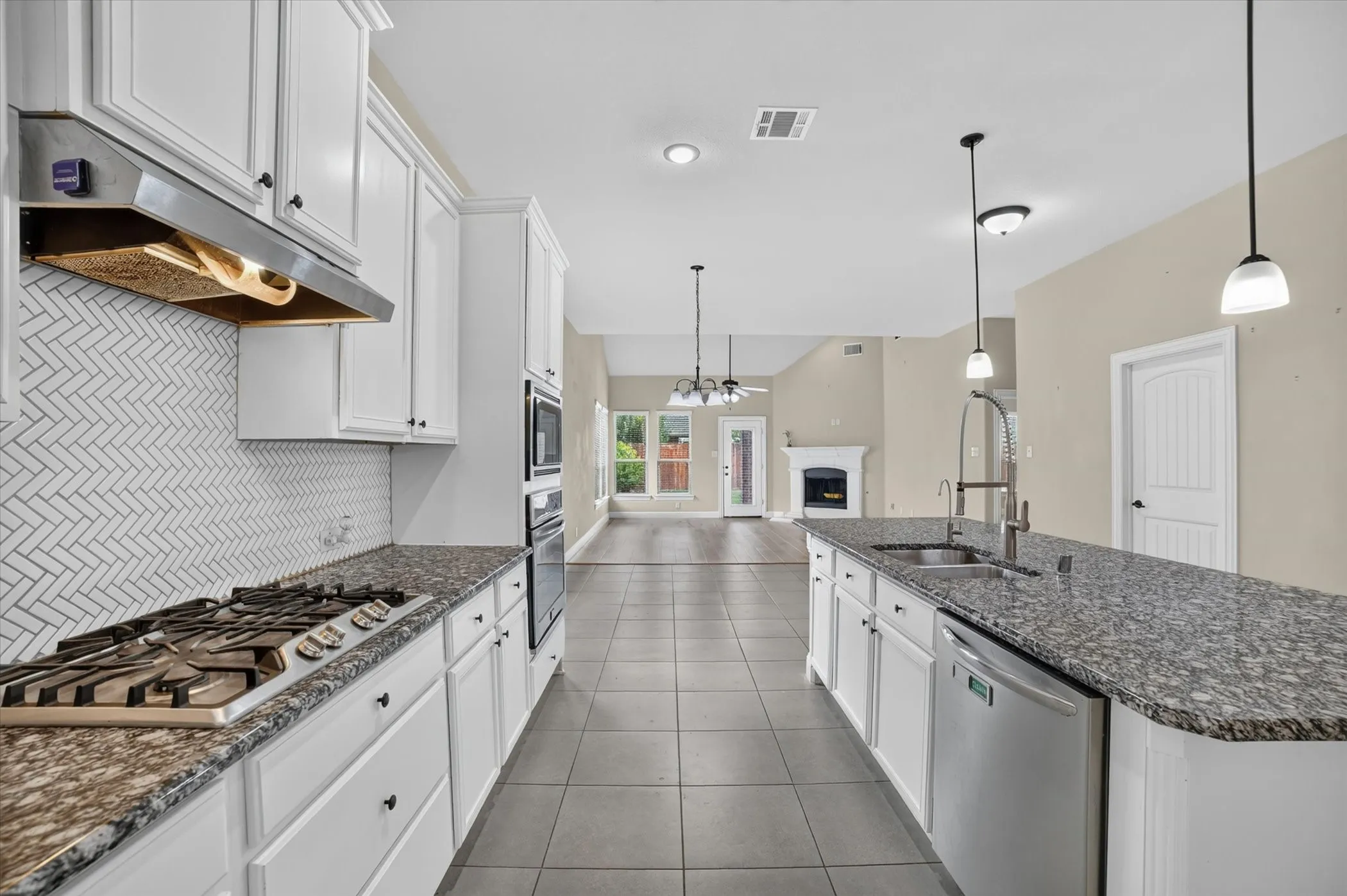 Modern kitchen featuring white cabinetry, stone countertops, a herringbone tile backsplash, and stainless steel appliances